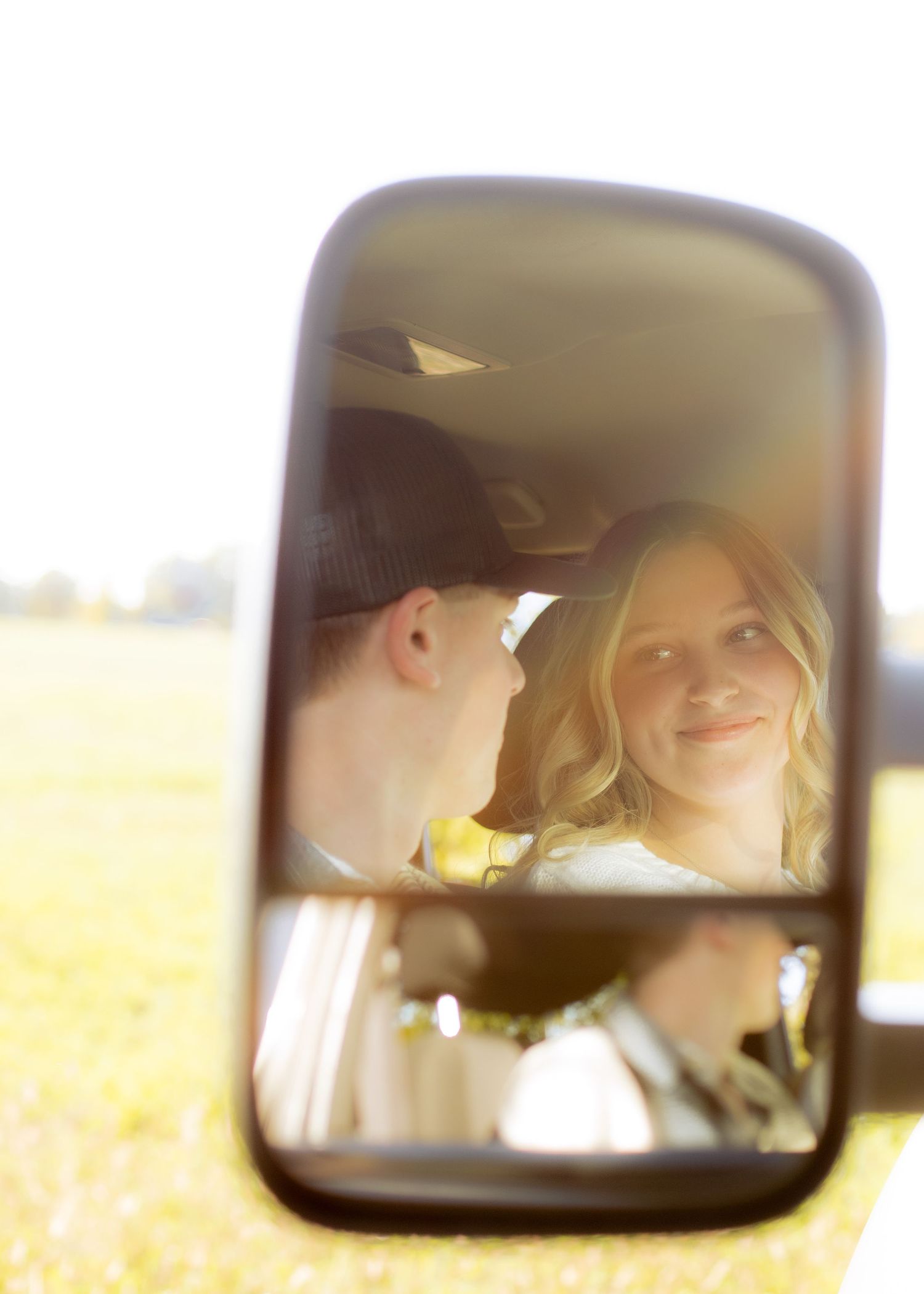 Couple reflected in a truck side mirror smiling at each other in bright sunlight.