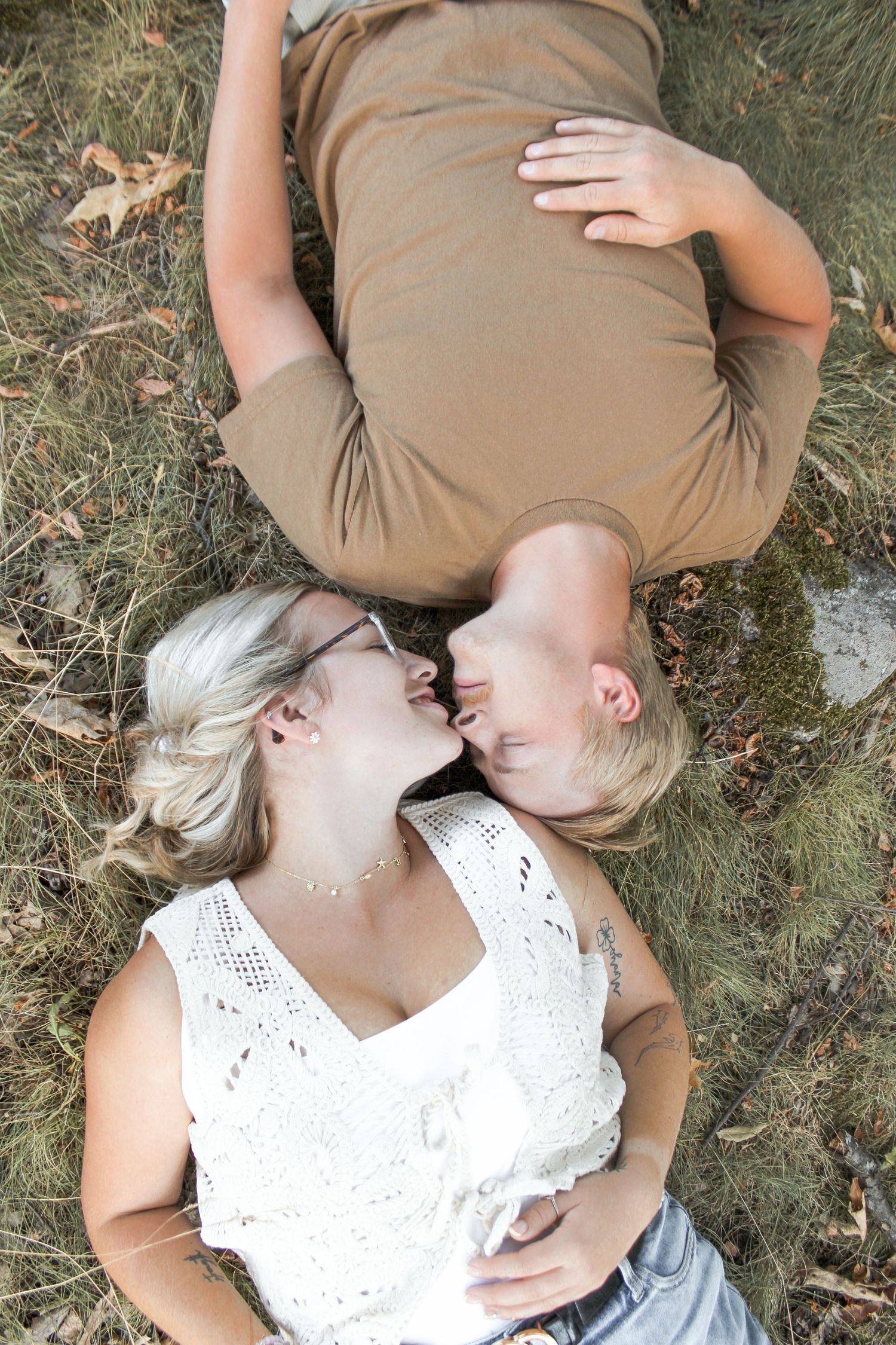 Couple lying in grass facing each other about to kiss during outdoor engagement photo session.