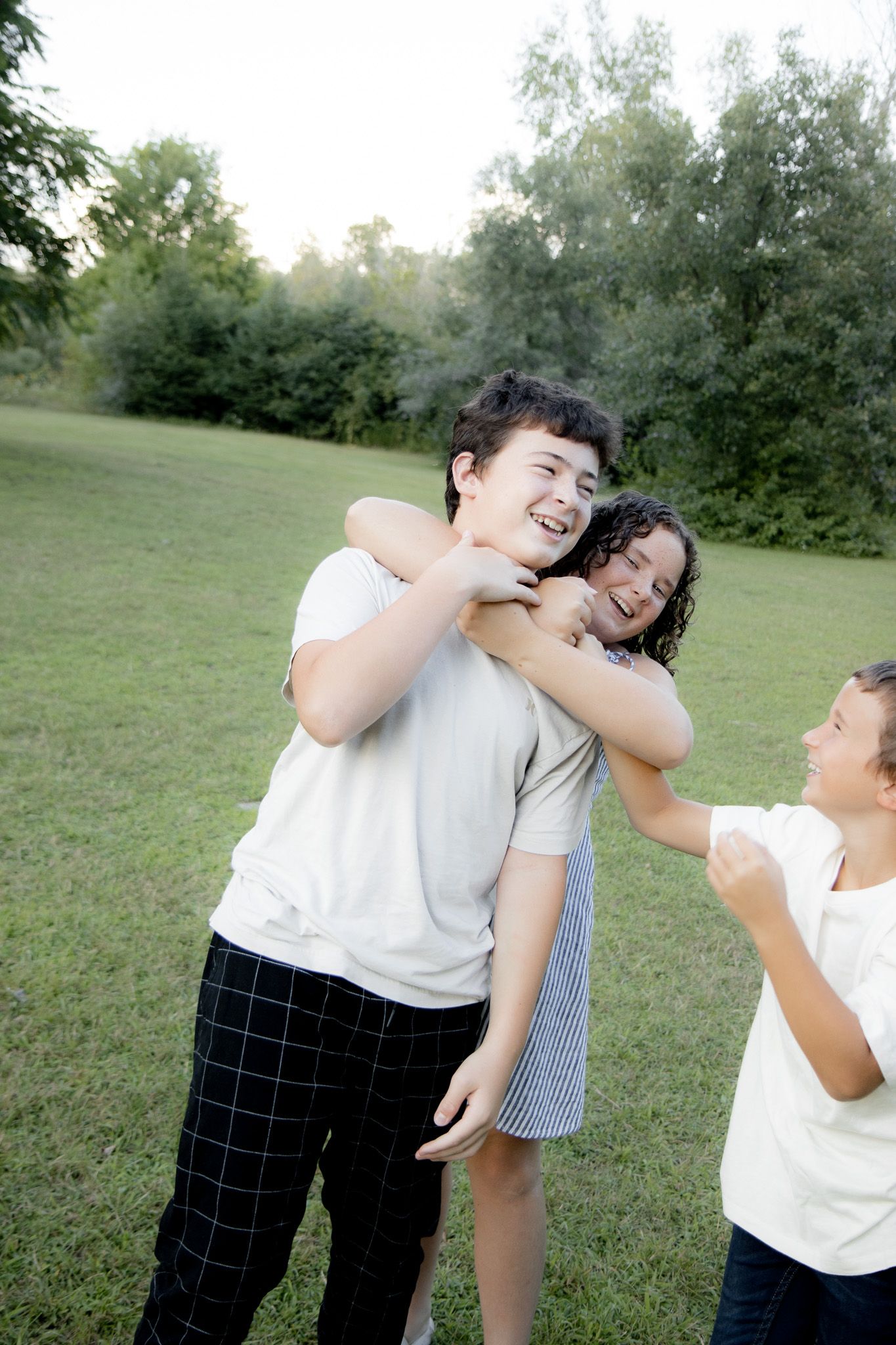 Three kids playing and laughing together outdoors in a green park on a sunny day.