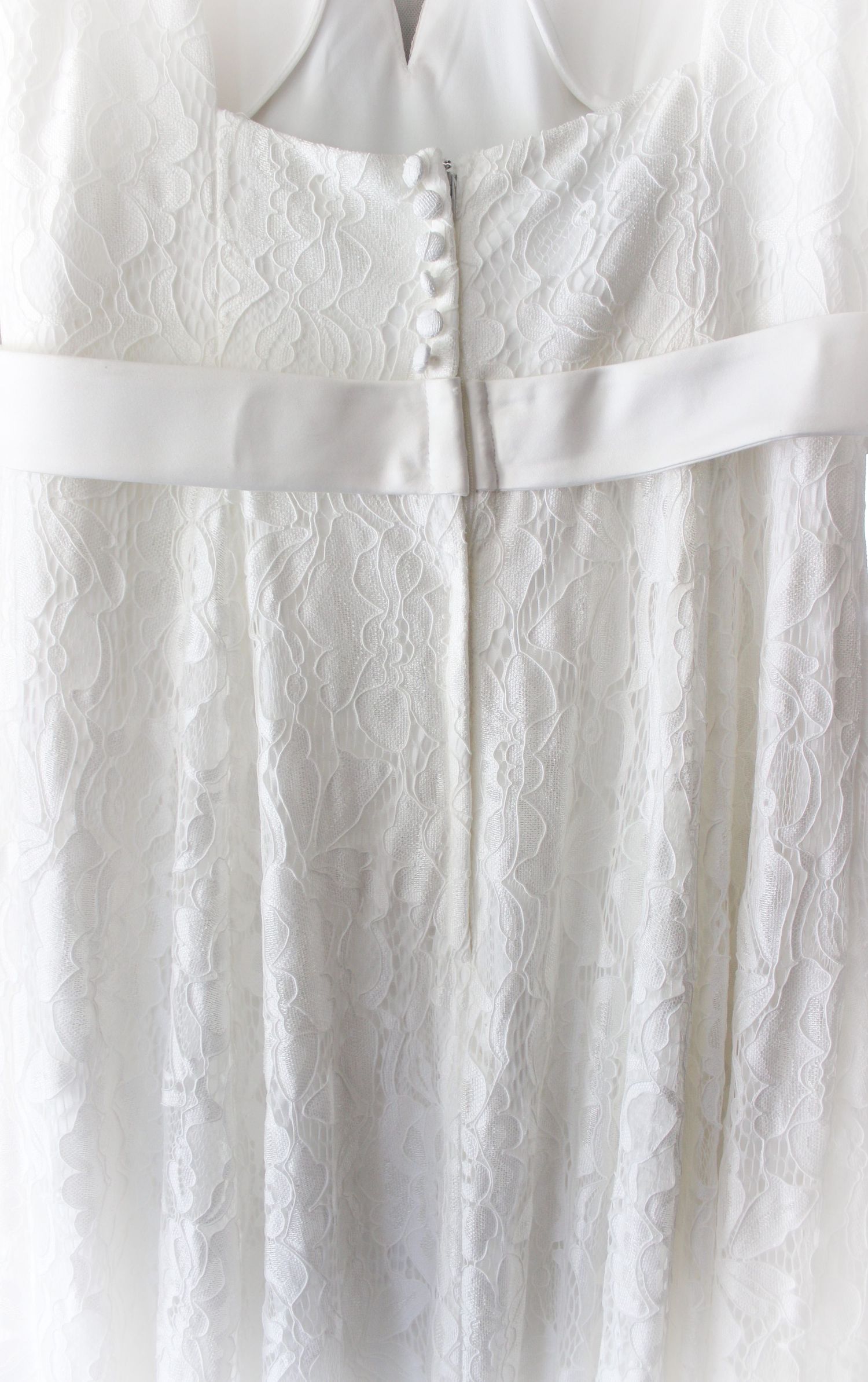 Close-up detail of white lace wedding dress with satin ribbon belt and pearl buttons.