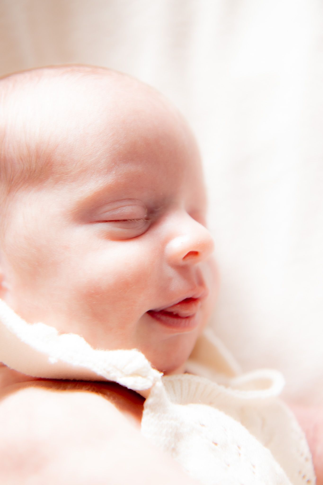 Peaceful sleeping newborn baby in white knit outfit with soft natural lighting.
