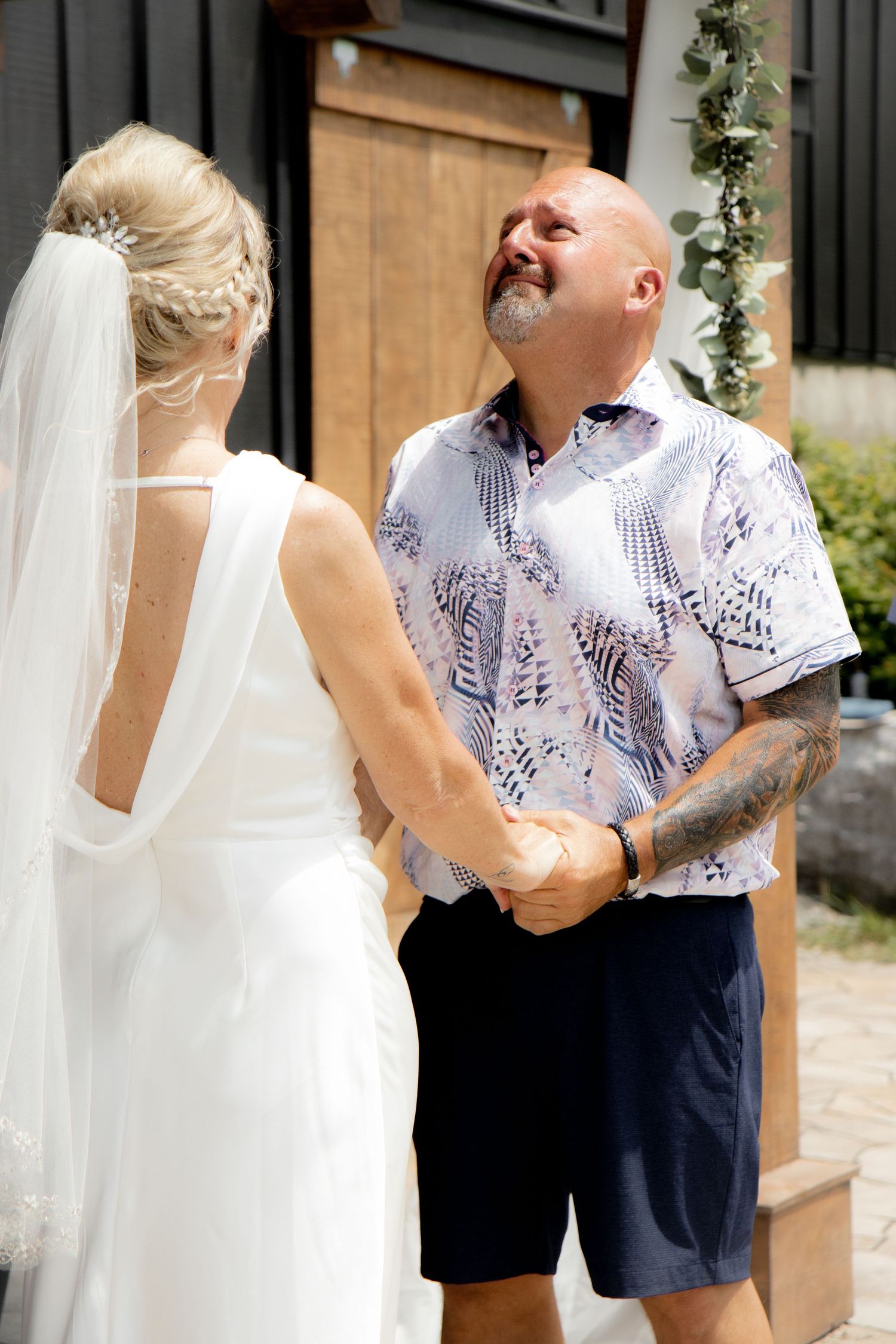 Emotional groom in patterned shirt reacts with joy seeing bride in white wedding dress and veil during outdoor first look.