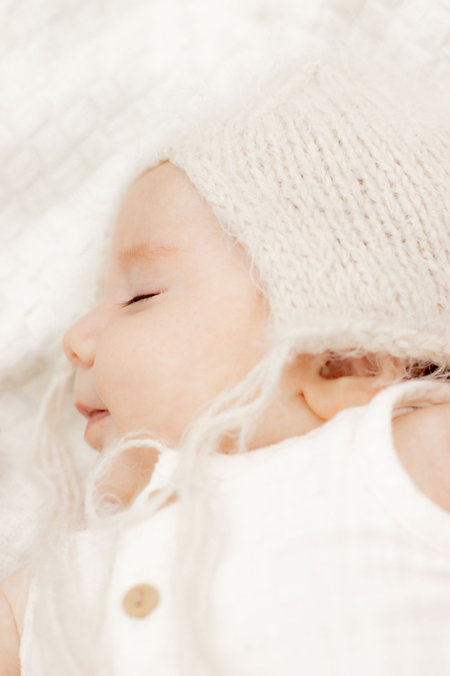 Peaceful sleeping newborn baby wearing a knit bonnet hat on a soft white blanket.