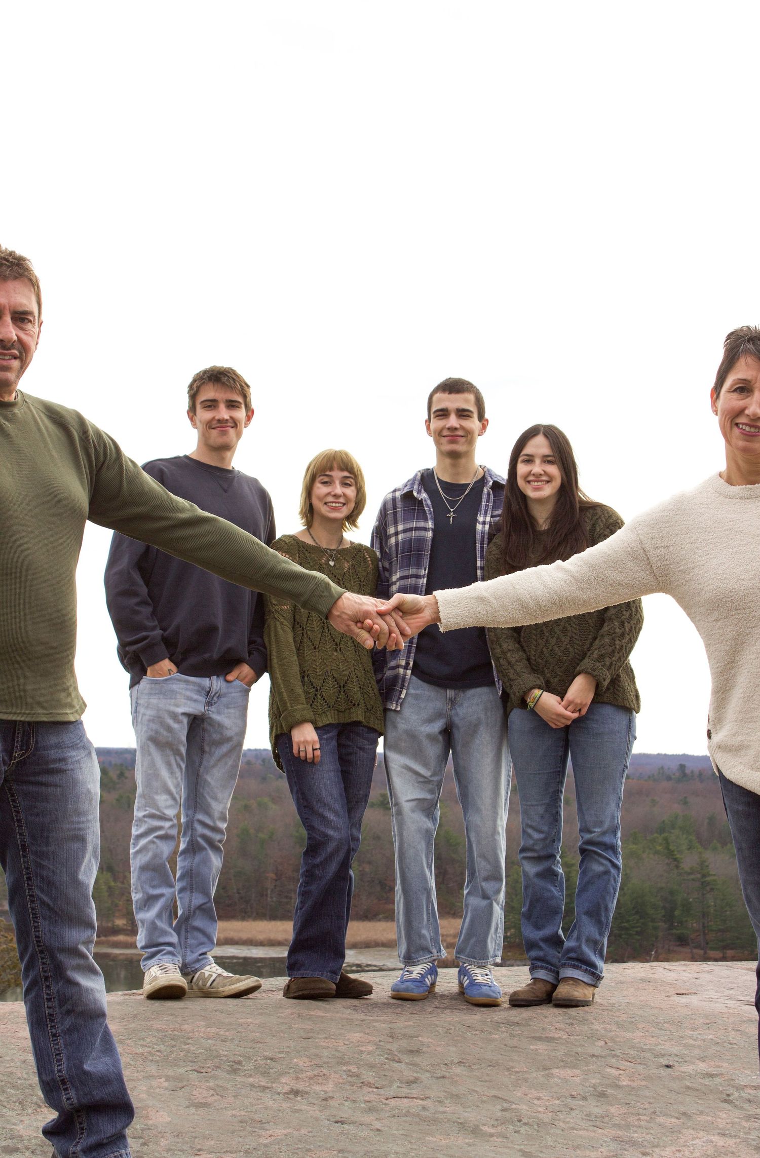 Family of six on rocky overlook, two adults extending hands to meet in center with four teens behind them.