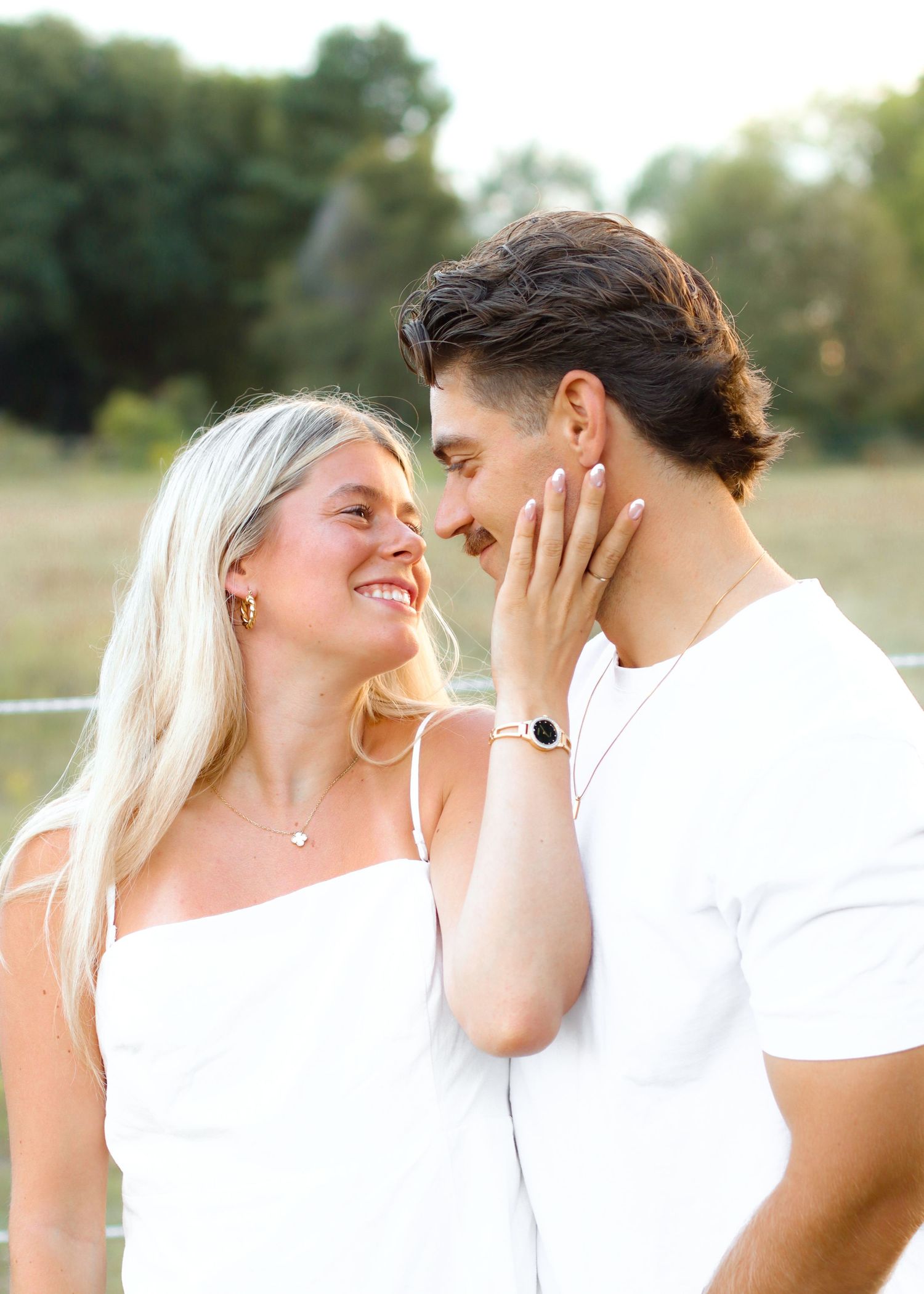Happy couple sharing a tender moment outdoors, smiling woman in white dress touches mans face.