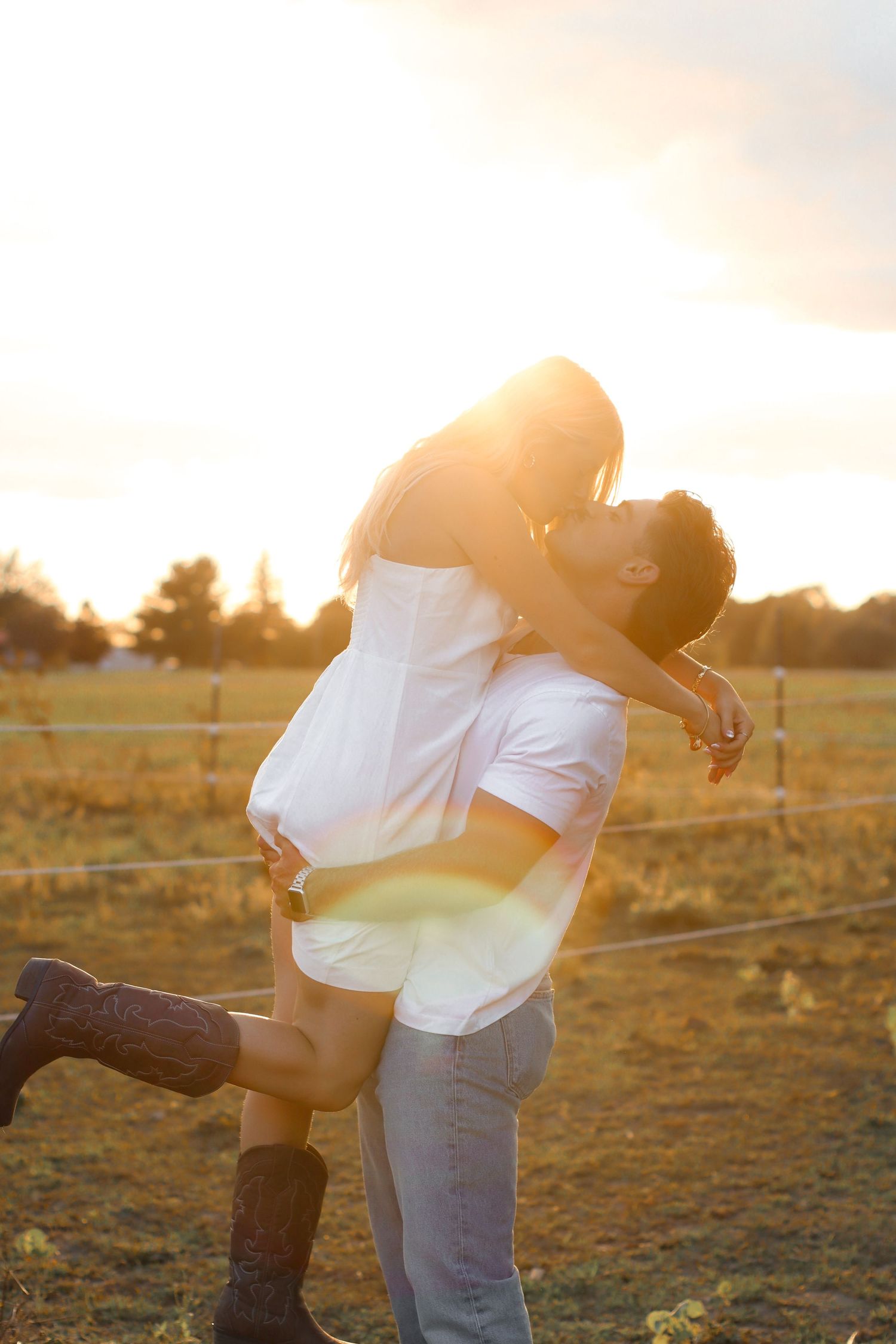Man lifting woman at golden sunset in farm field, couple sharing joyful romantic moment.