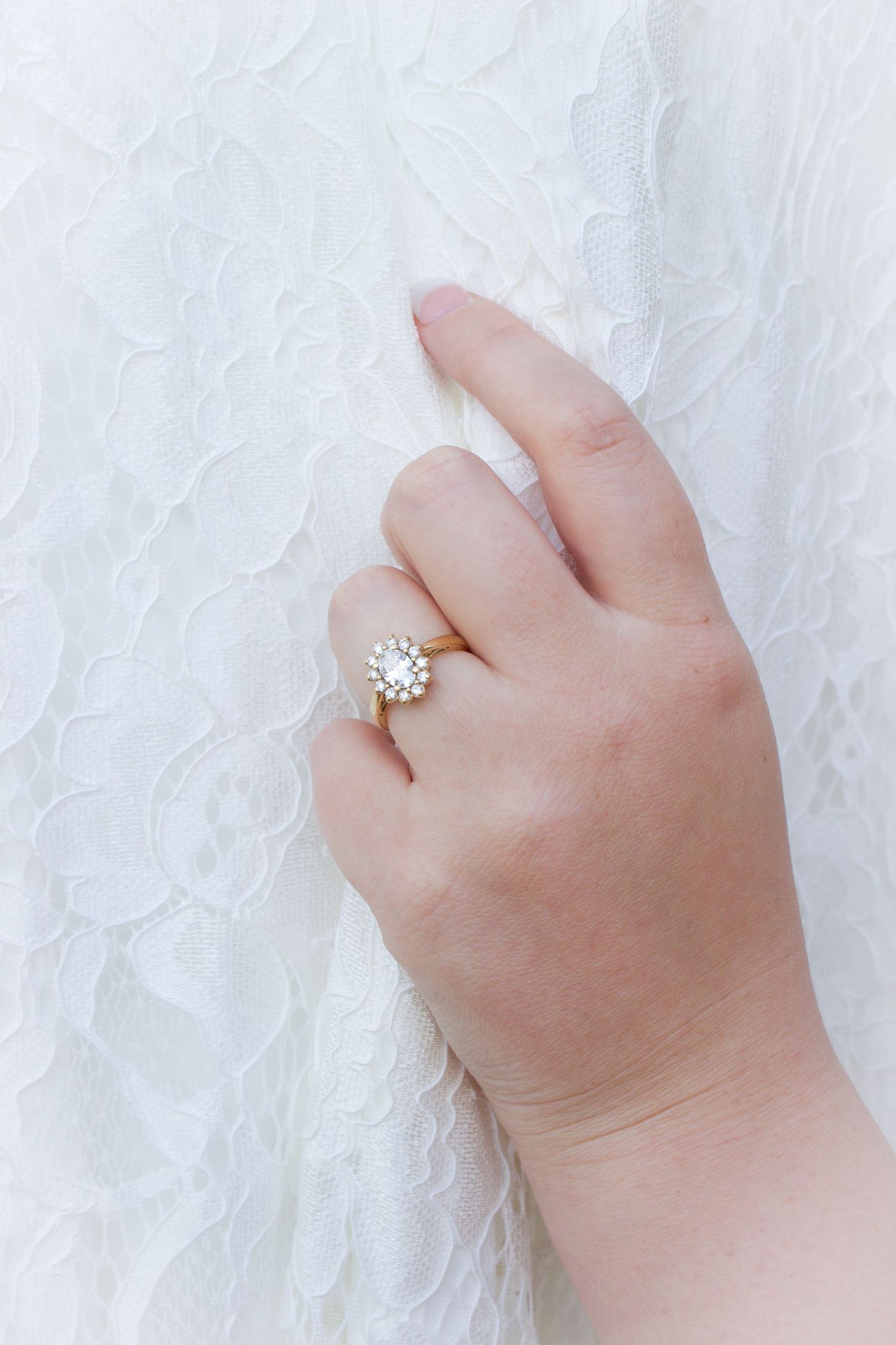 Bride wearing gold diamond halo engagement ring while holding white lace wedding dress.