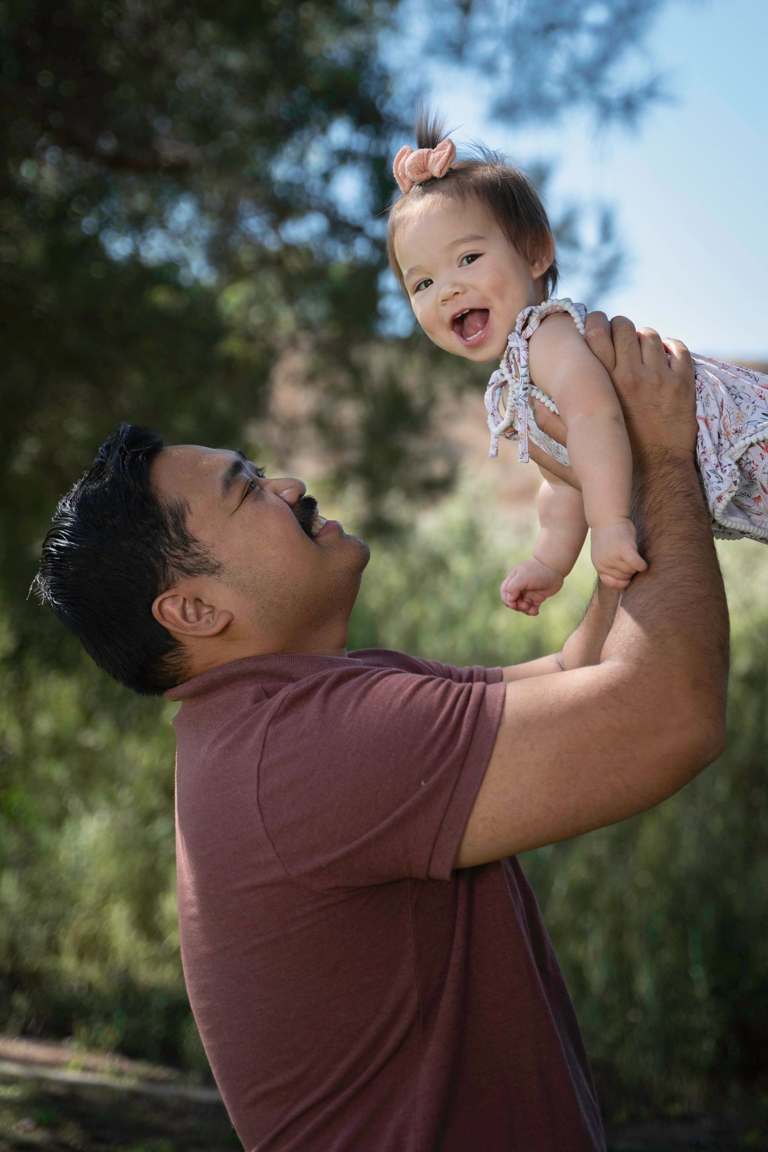 Playful moment captured as a parent lifts and plays with a small child against a blue sky.
