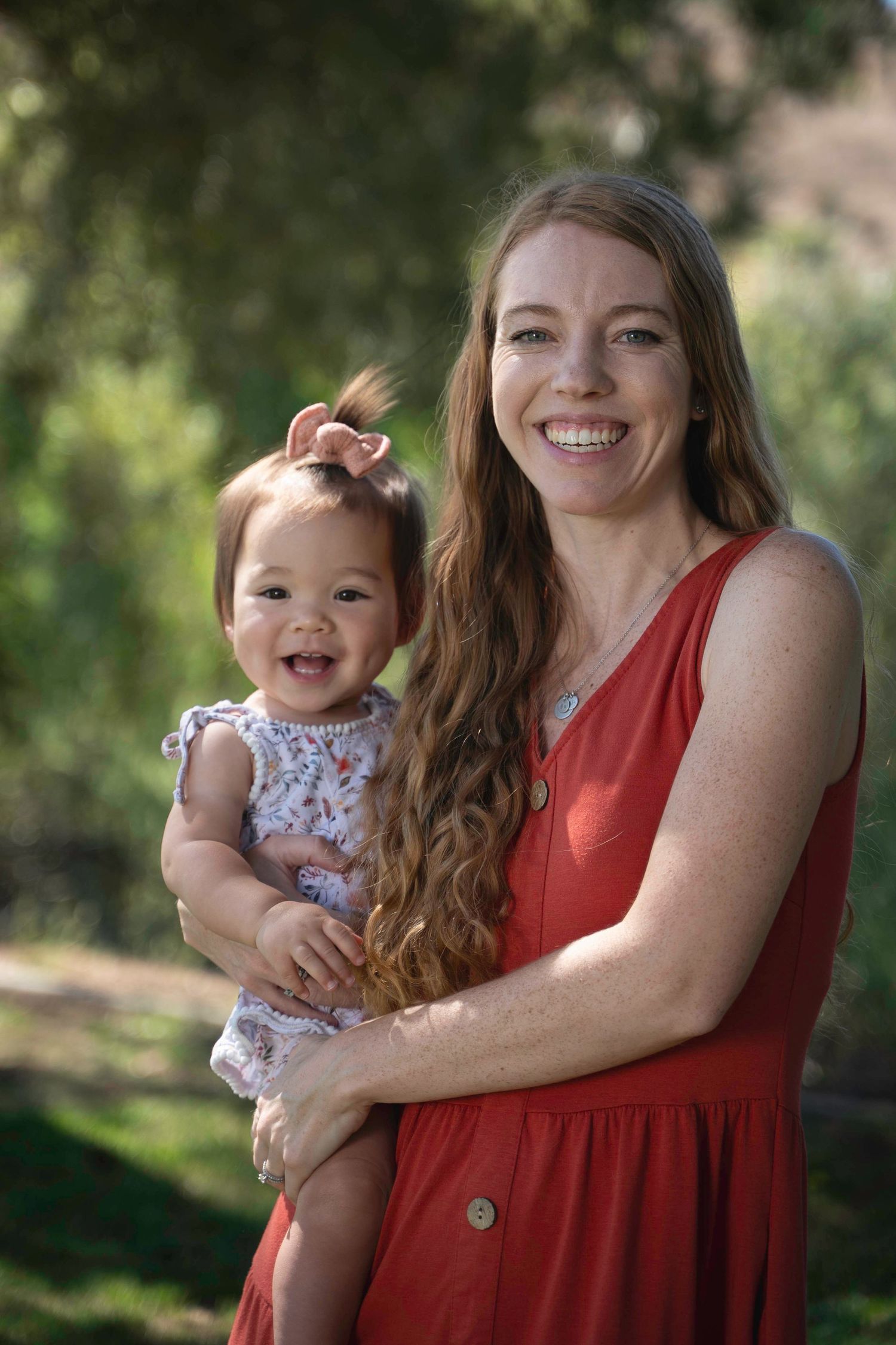 A tender parent-child moment captured outdoors in a red dress against a natural backdrop.