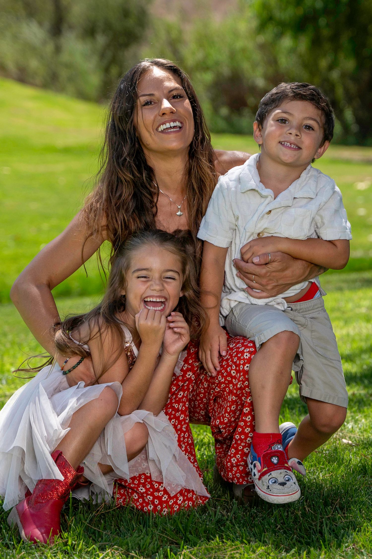 A joyful family sits together on green grass outdoors, wearing red polka dot dress and white outfits.