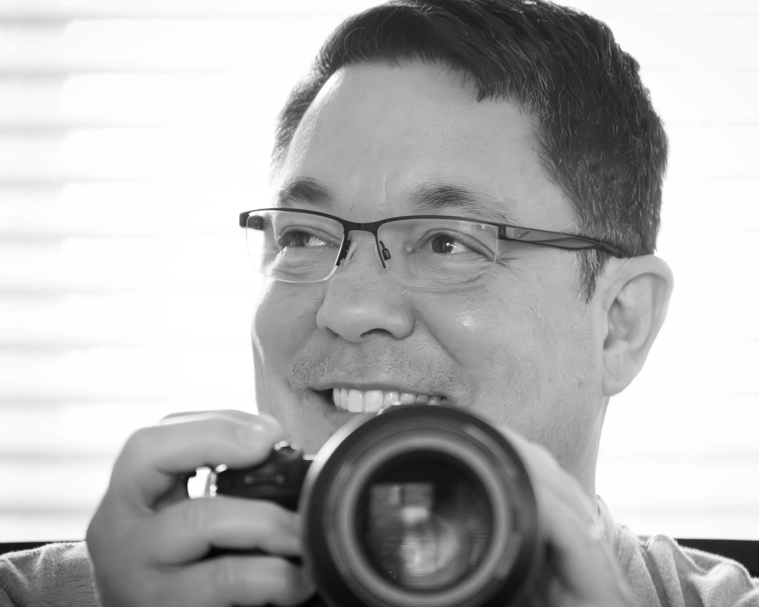 Black and white close-up shot of someone smiling while holding a camera.