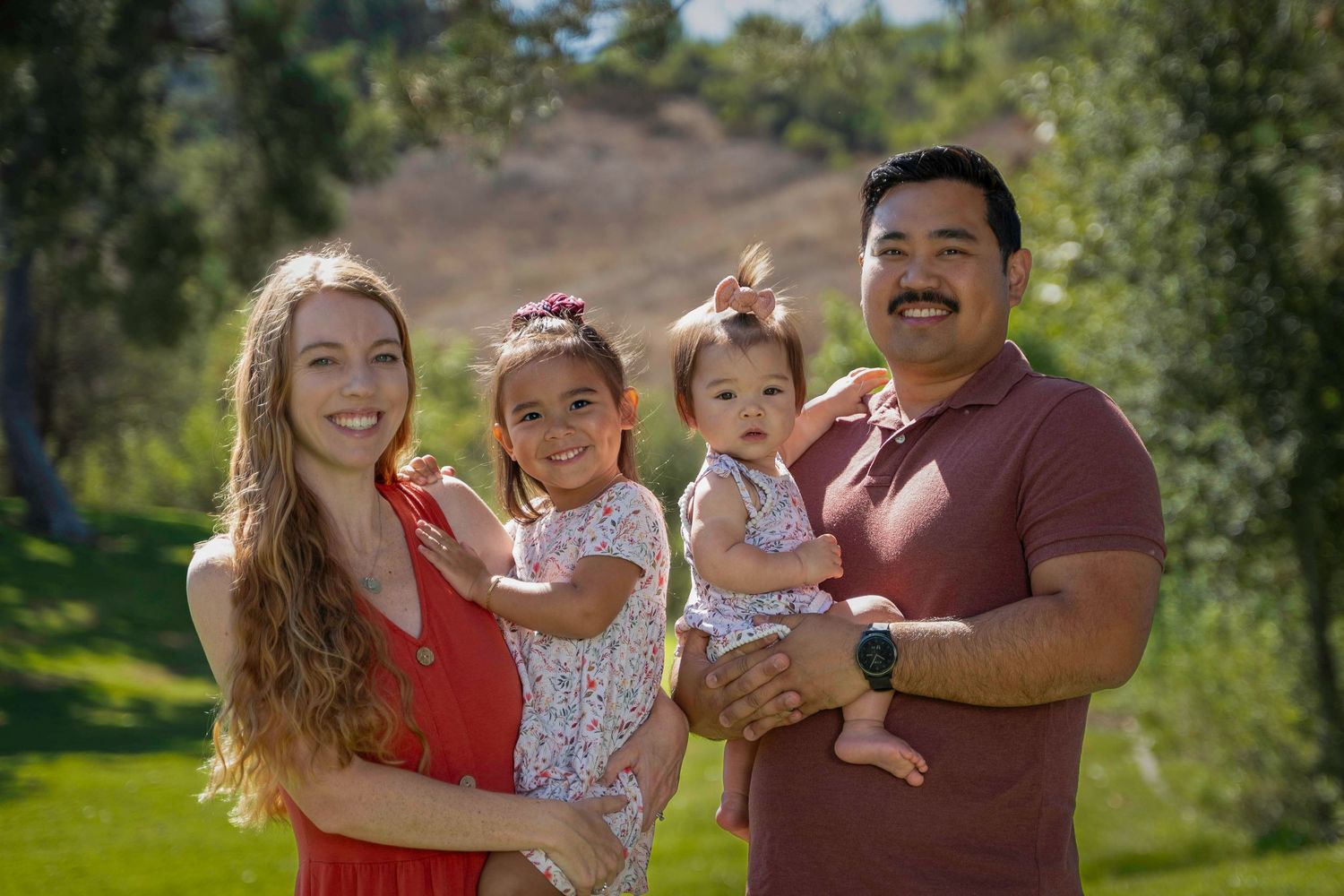 Happy family poses together in a natural outdoor setting with trees in the background.