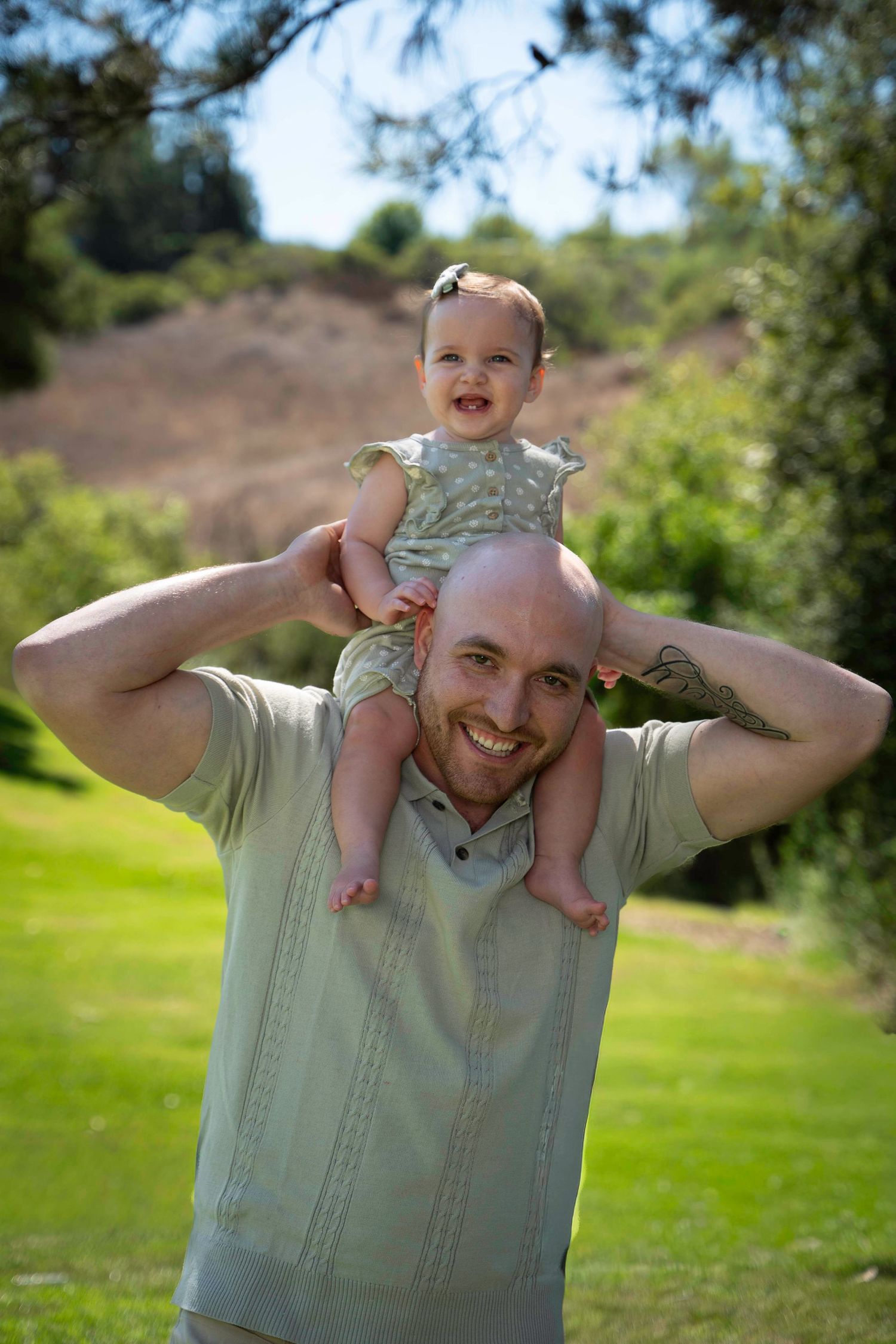 Parent lifting small child playfully in the air on a sunny day in a grassy area.