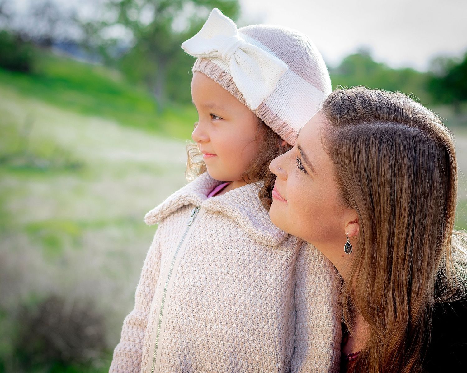 Family members share a close moment outdoors wearing white knit sweaters.
