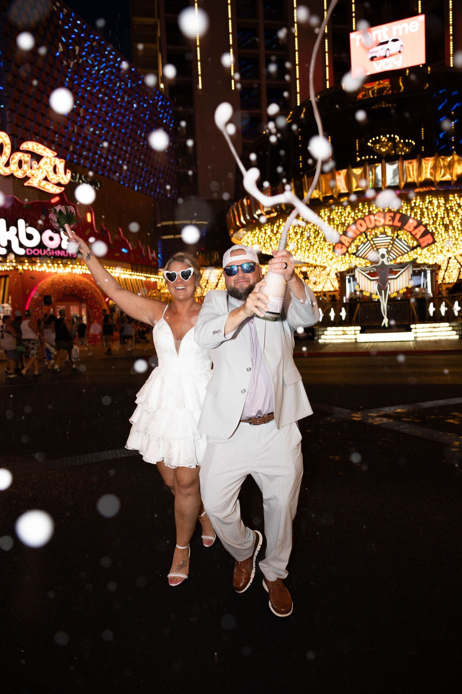 A playful Las Vegas elopement photoshoot featuring a bride and groom in stylish wedding attire under the bright casino lights with champagne