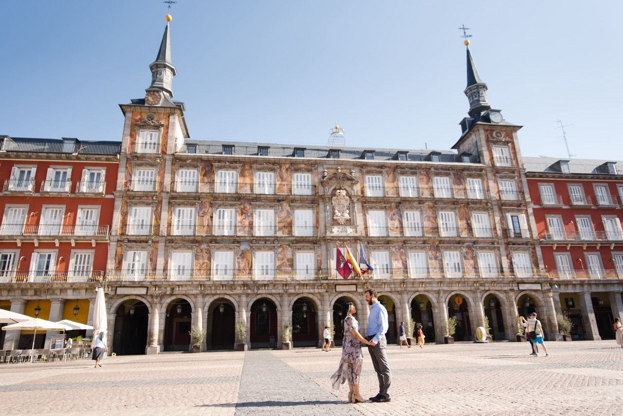 Couple embracing in front of the historic Plaza Mayor building in Madrid with its distinctive architecture.