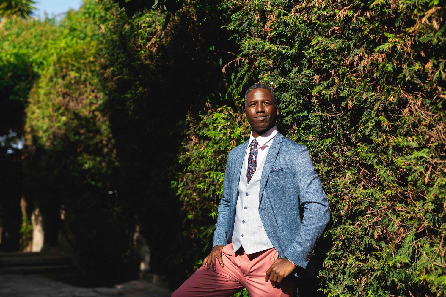 A stylishly dressed photographer in a light blue blazer and burgundy pants on a sunny day.