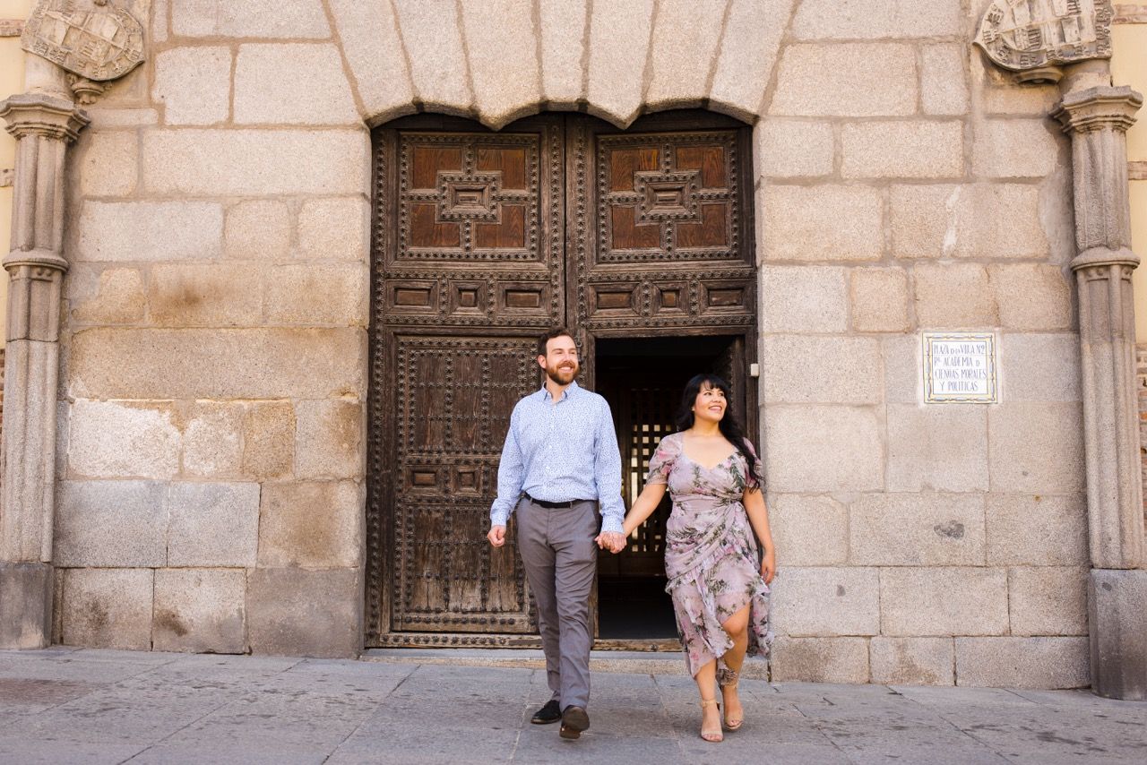 Couple walking hand in hand through an ornate medieval doorway entrance in downtown madrid.