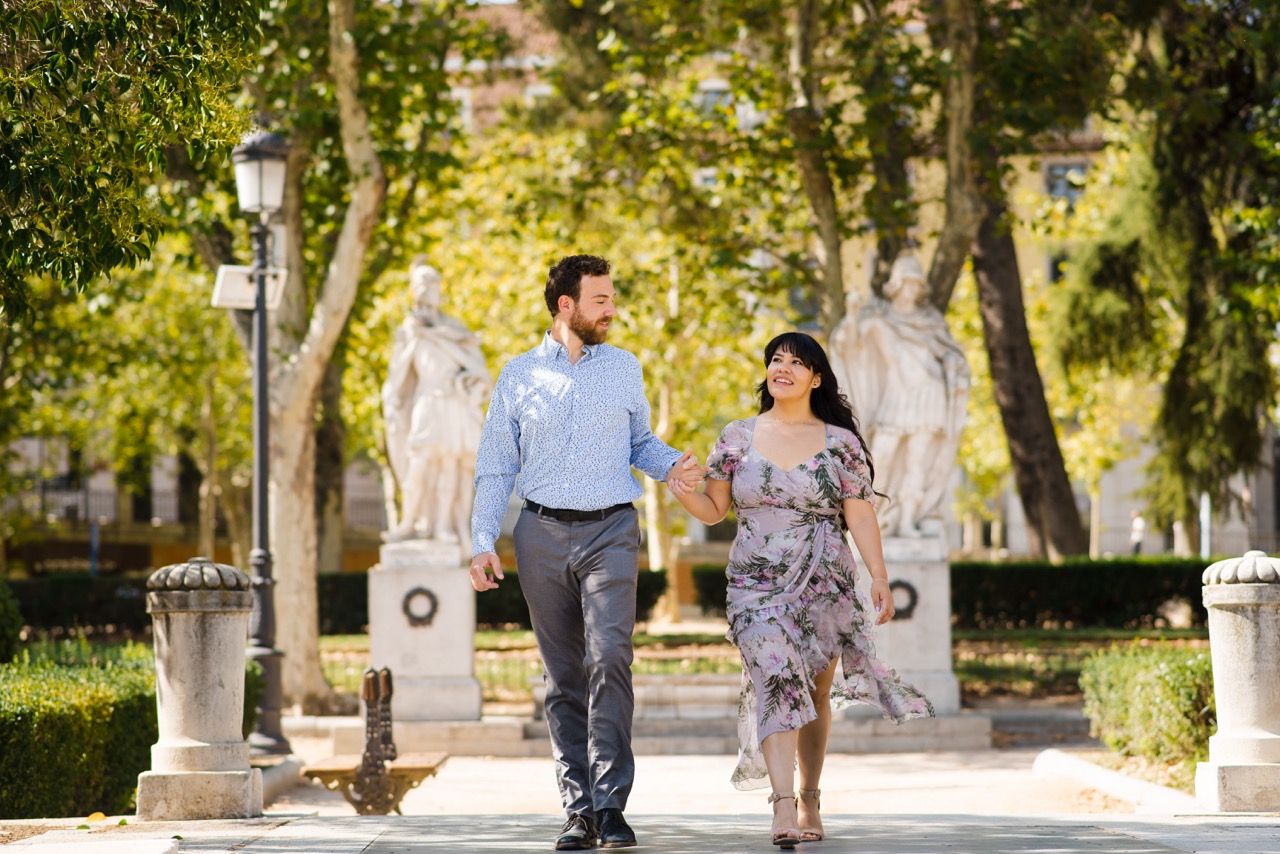 Couple walking together through a tree-lined park pathway on a sunny day.