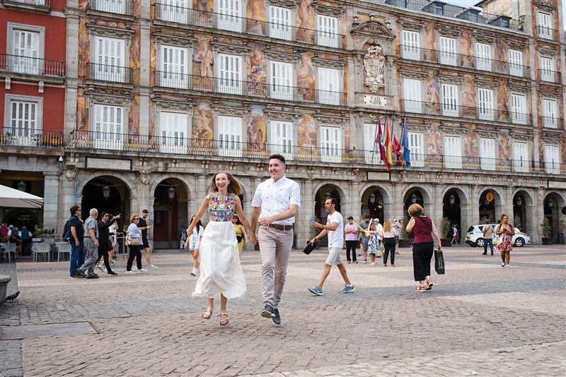 People walking along the historic Plaza Mayor with classic Spanish colonial architecture in Madrid, Spain.