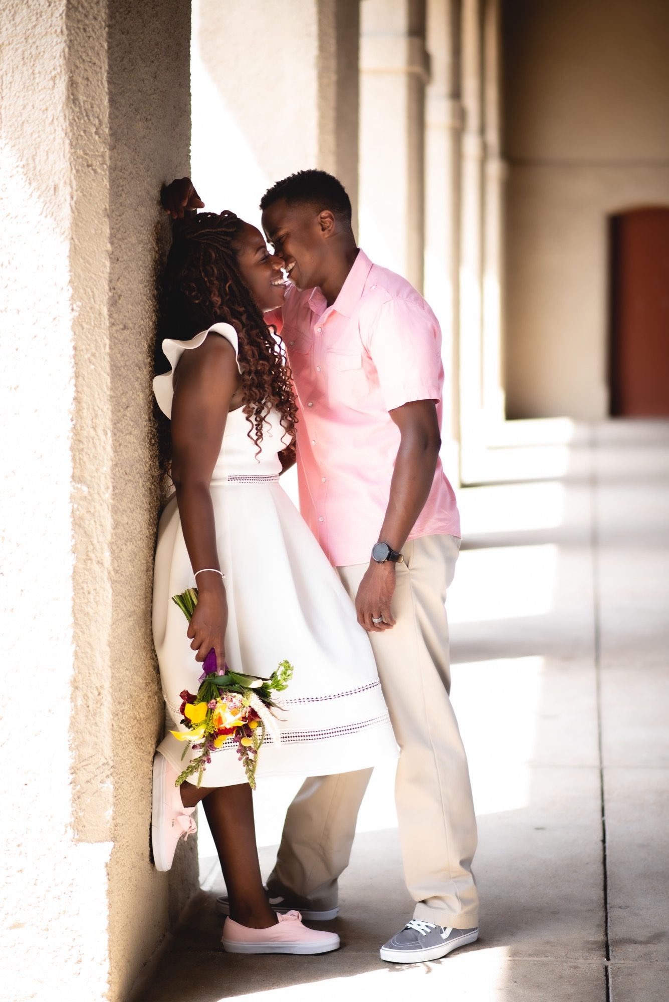 Couple sharing an intimate moment in a columned hallway with yellow flowers during a couples engagement photography session in Spain.