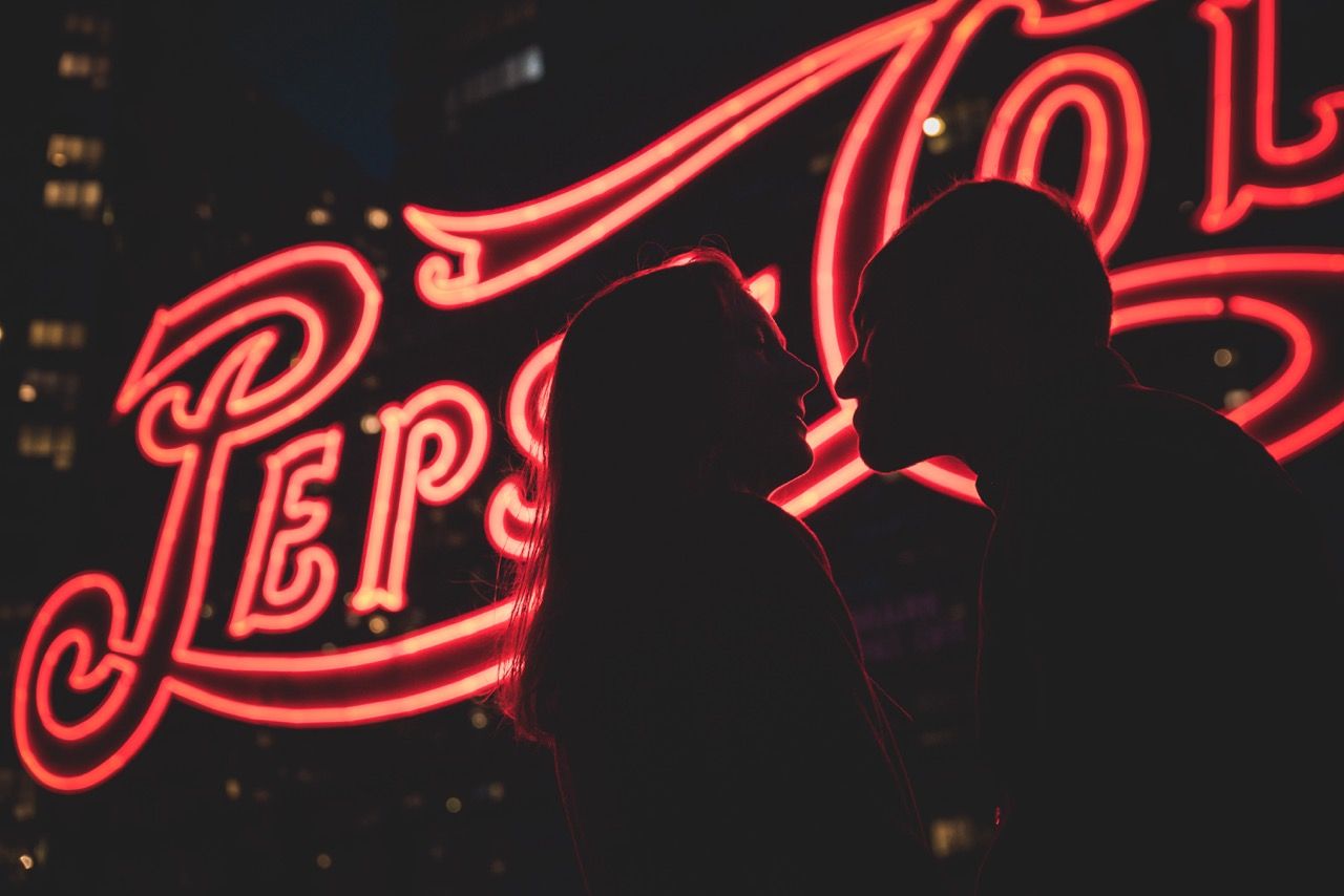 Red neon signs glowing against dark background with cursive text and decorative elements.