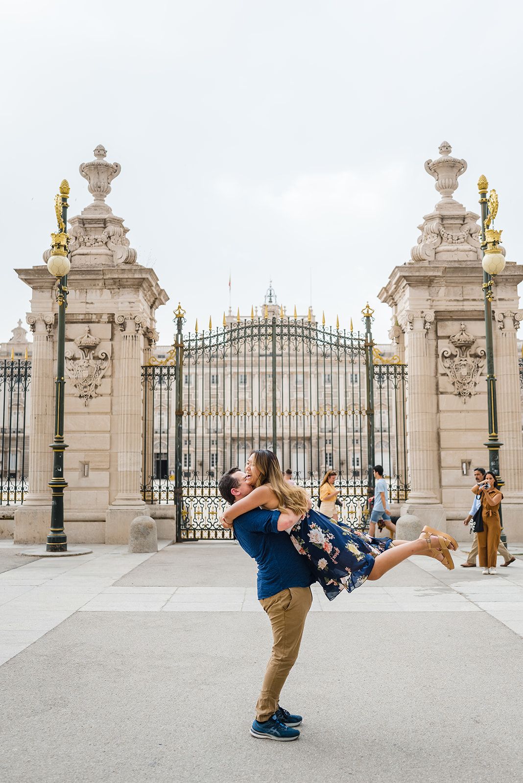 Joyful lifting pose in front of ornate Madrid Royal Palace gates with golden decorative elements.