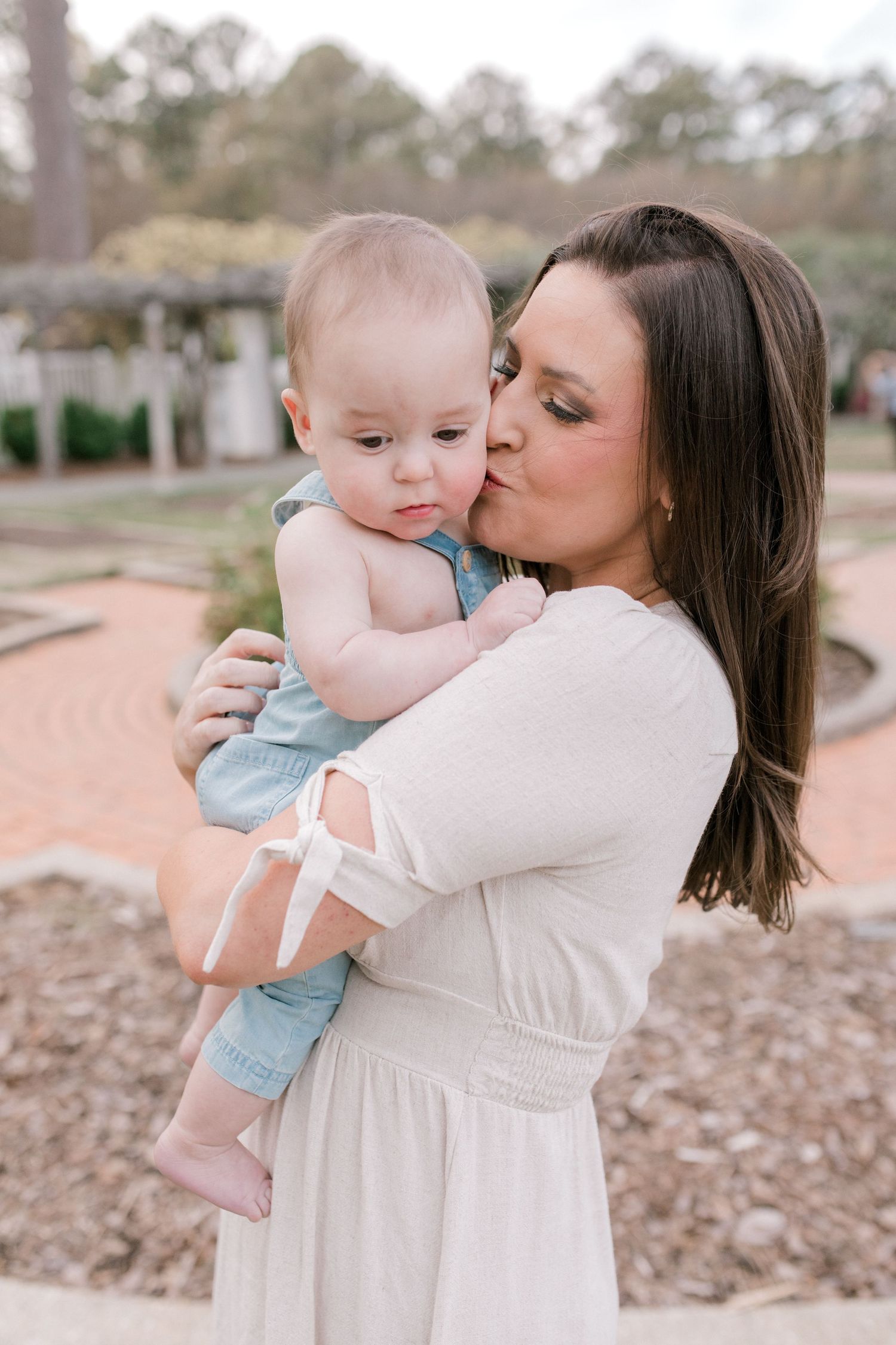 A tender moment outdoors as parent and infant share a sweet embrace in a garden setting.