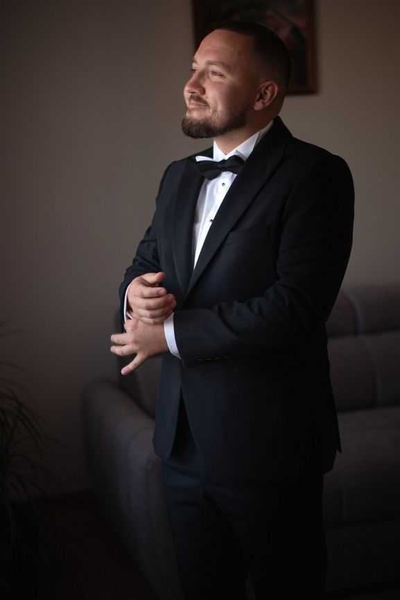 Pan młody stoi przed oknem.