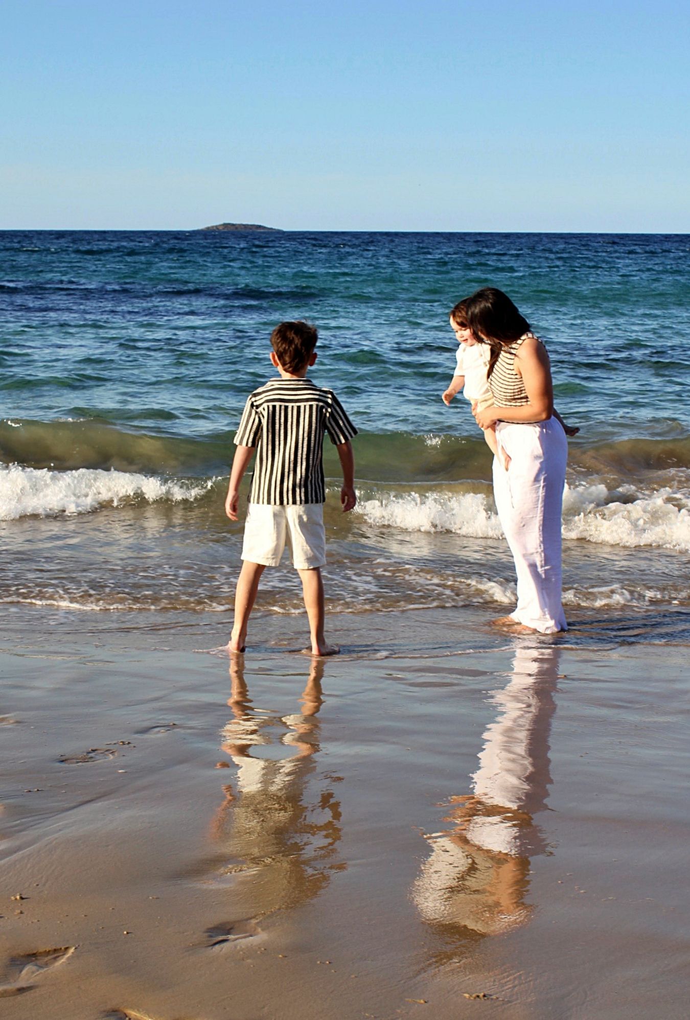 Mother and son sharing a playful moment in the water, captured from behind during a candid beach session.