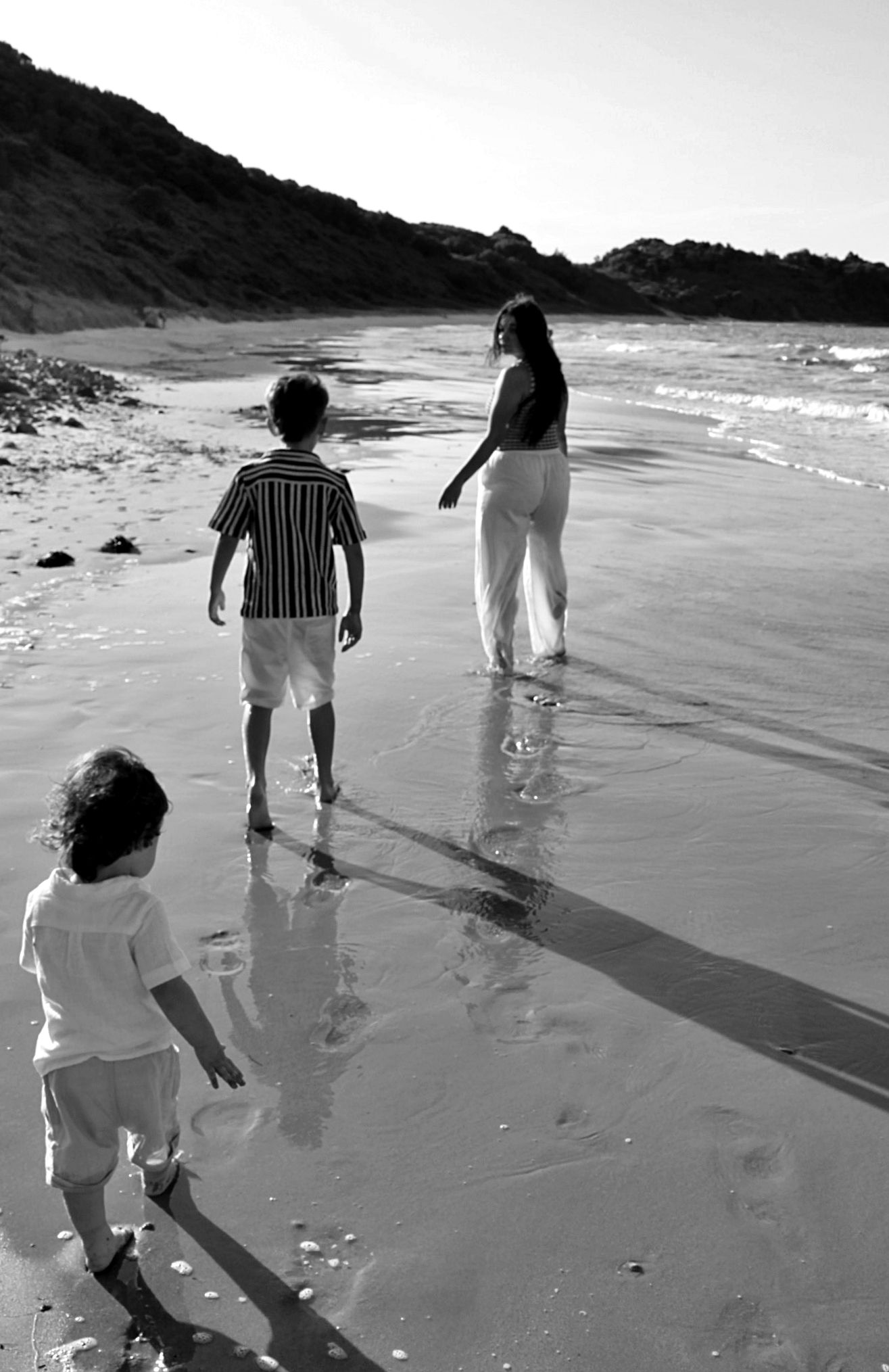 Mum running along the beach with her two children chasing her capturing a candid playful moment during a motherhood session.