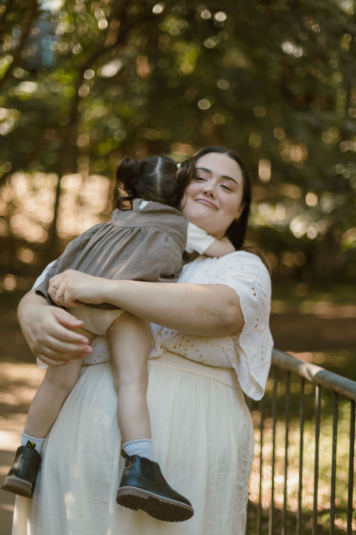 Mum wrapping her arms around her young daughter during a warm candid family moment.