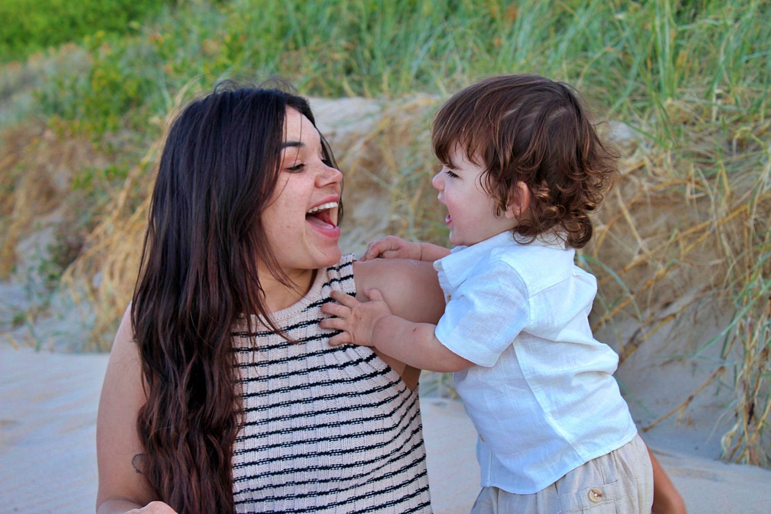 Mother smiling at her son while he looks at her during a beach motherhood session on the sand.