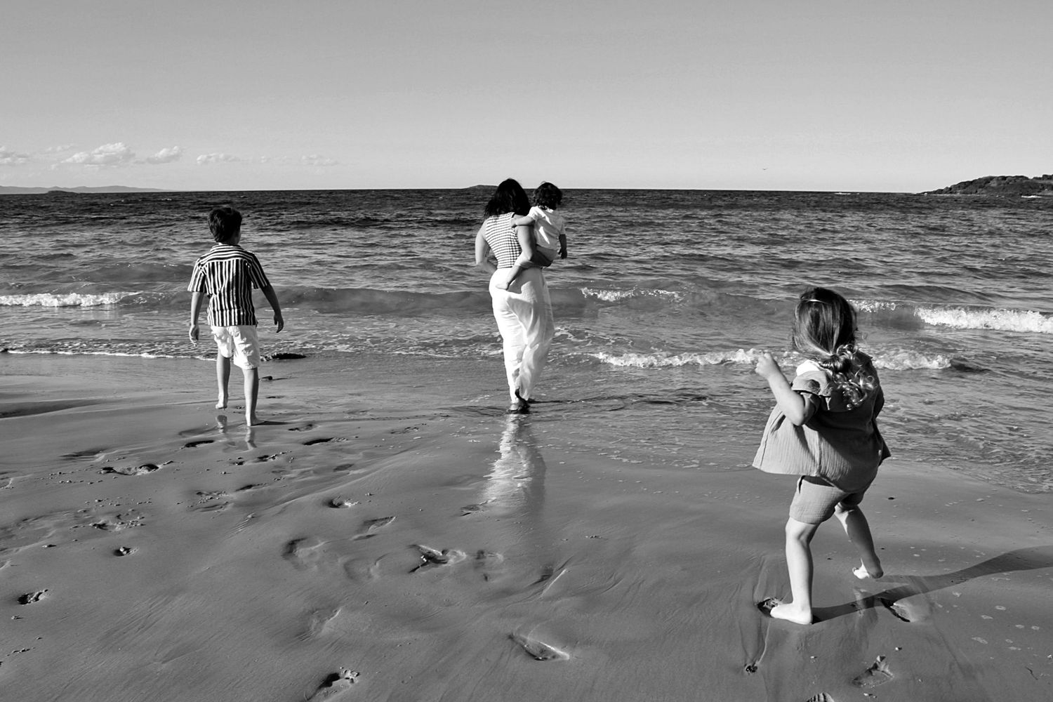 Candid motherhood photography session on the beach featuring a mum and her three boys enjoying the shoreline together.