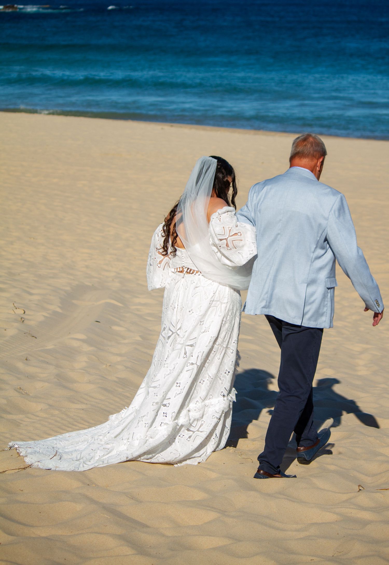 Behind view of the bride walking down the aisle with her father at an Illawarra beach wedding ceremony.