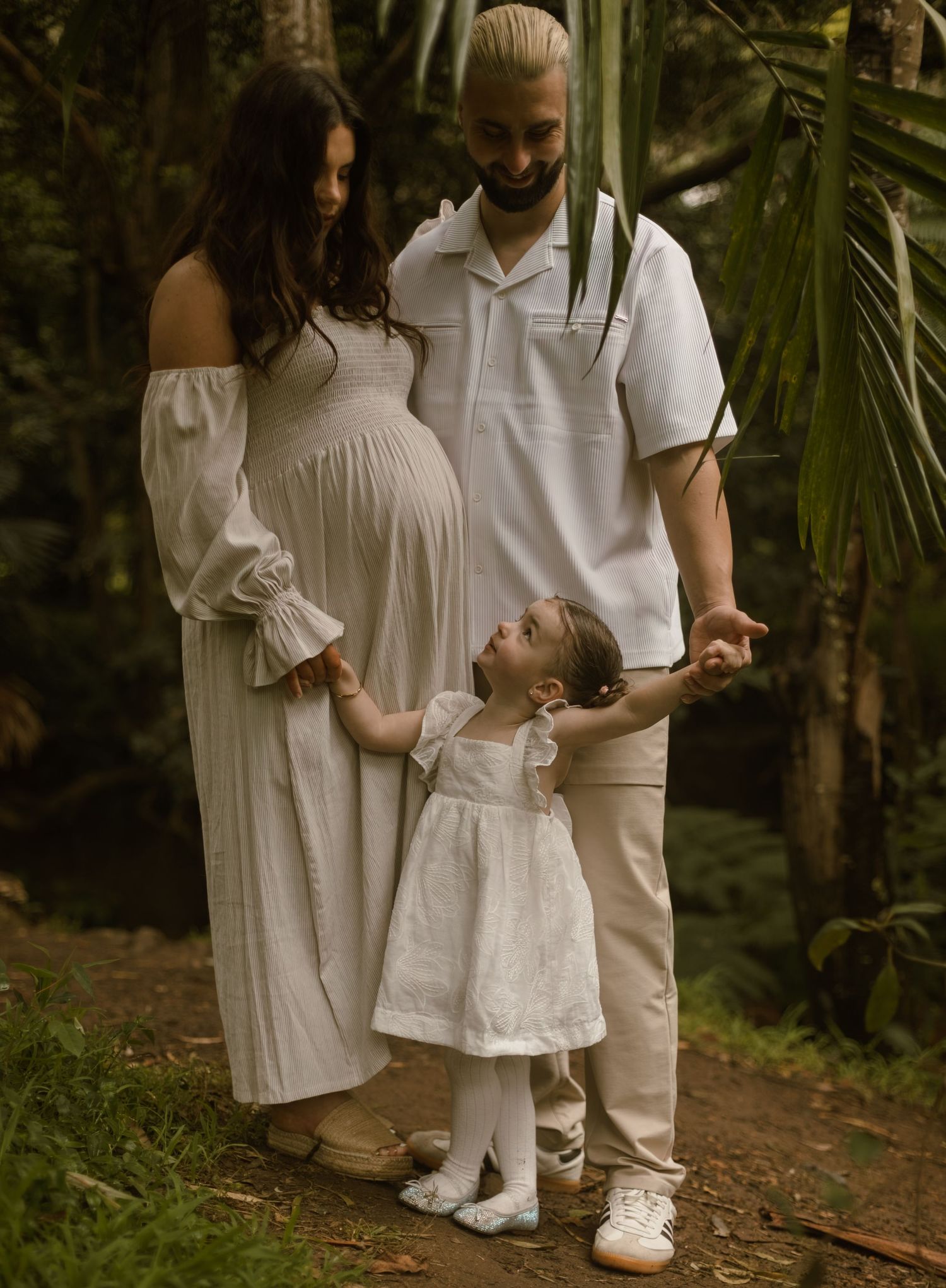 Mum and Dad holding hands with their young daughter during an outdoor family maternity photography session.