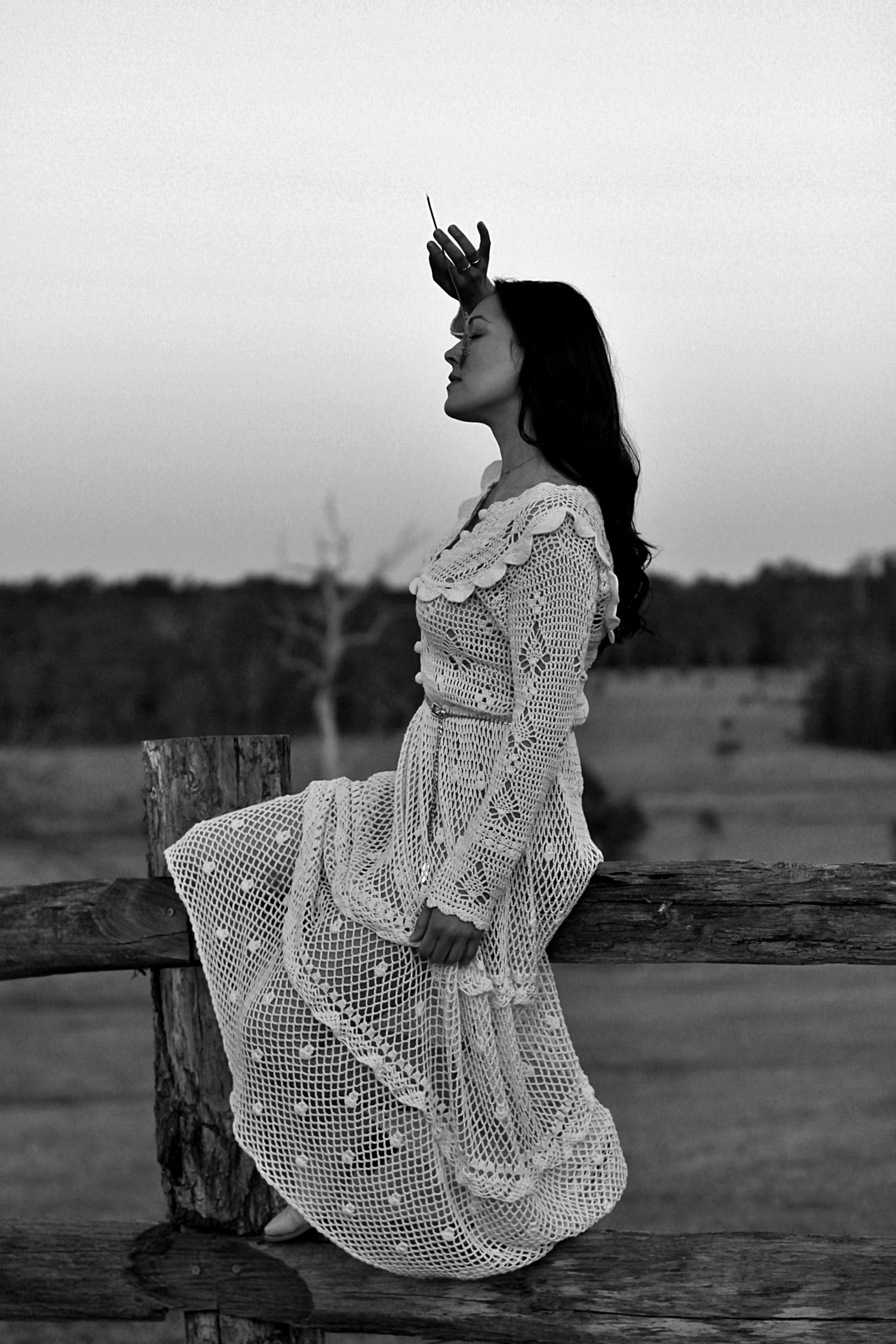 Woman sitting on a fence surrounded by nature in a rural setting