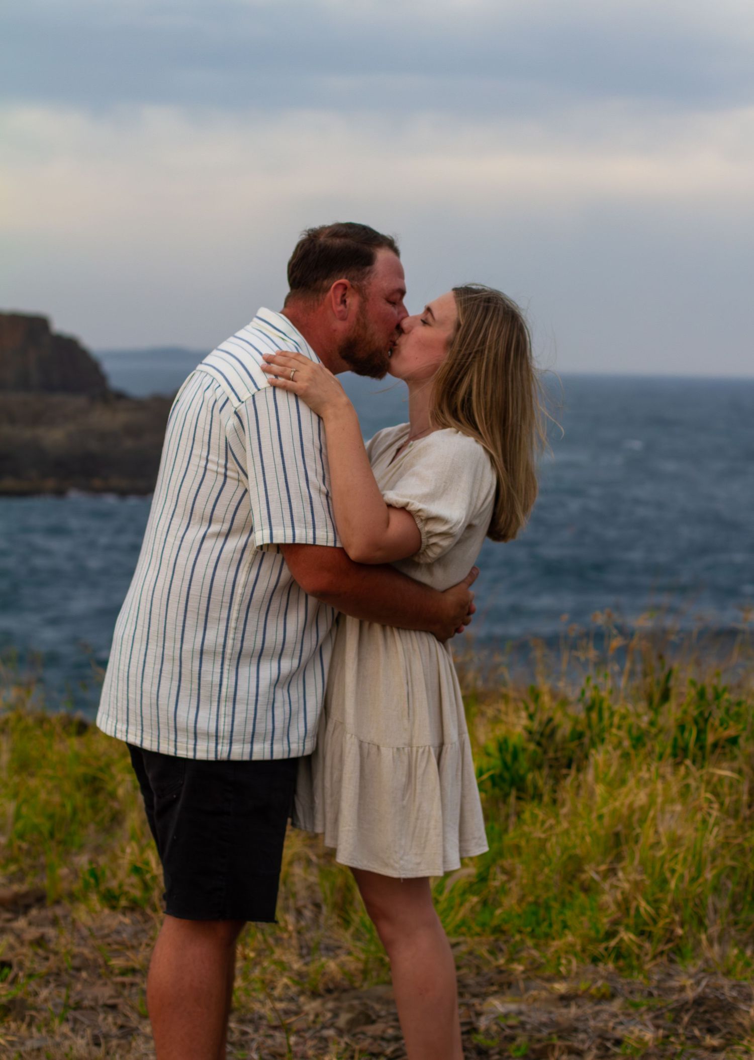 Couple sharing an intimate kiss at Bombo Quarry with ocean water and rugged rock formations in the background.