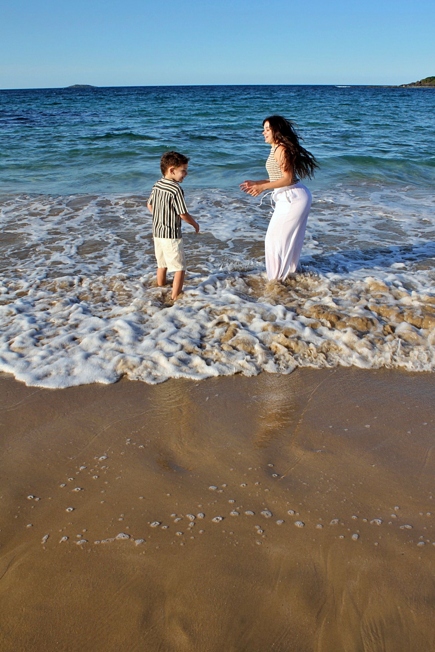 Mother and son sharing a playful moment in the water, captured from behind during a candid beach session.