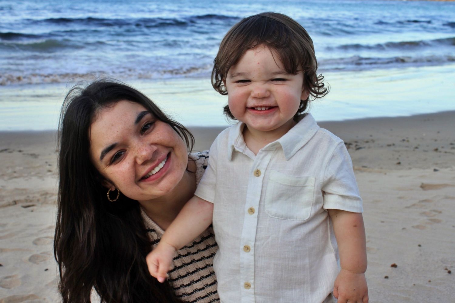 Mother and her young son smiling at the camera, sharing the same joyful smile during a beach motherhood session.