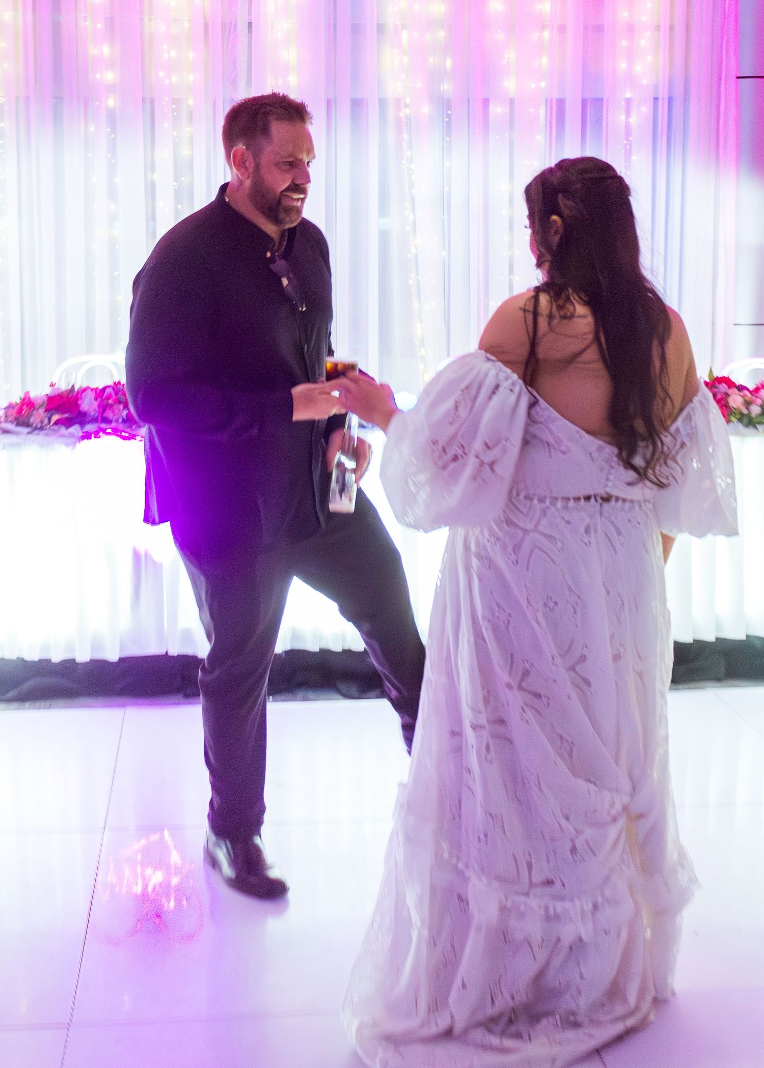 Candid wedding photo of the bride and groom dancing, with the groom smiling at his bride during their joyful celebration.
