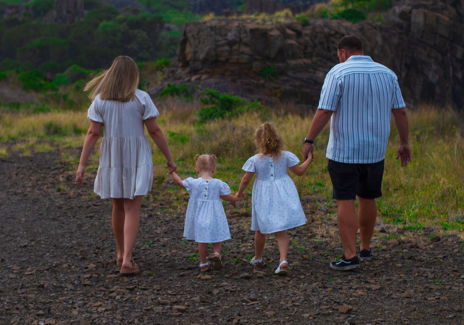Family walking hand in hand during golden hour, backlit by warm sunlight, captured by an Illawarra family photographer.