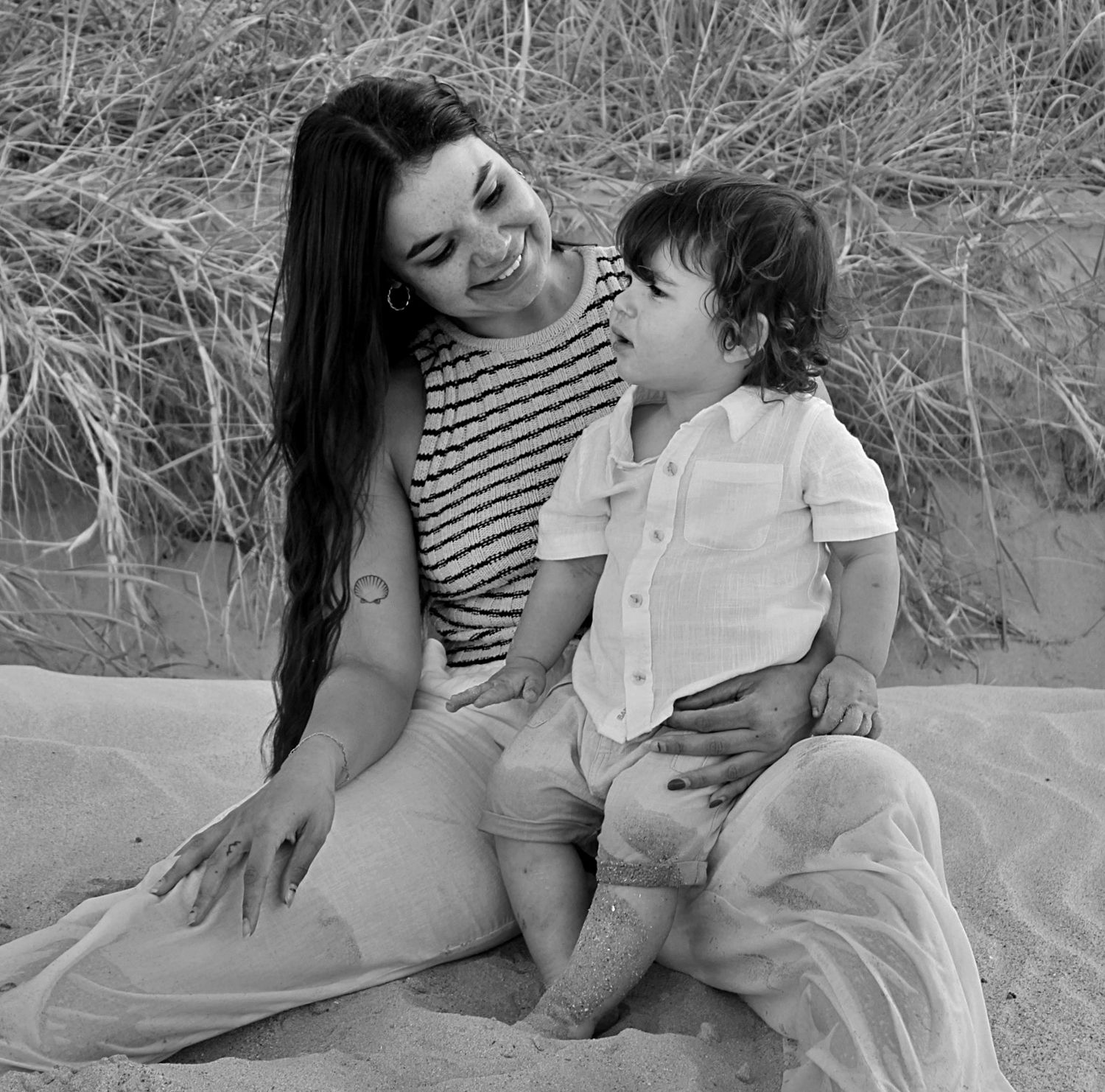 Mother and son looking at each other full of love while sitting on the beach during a motherhood session.