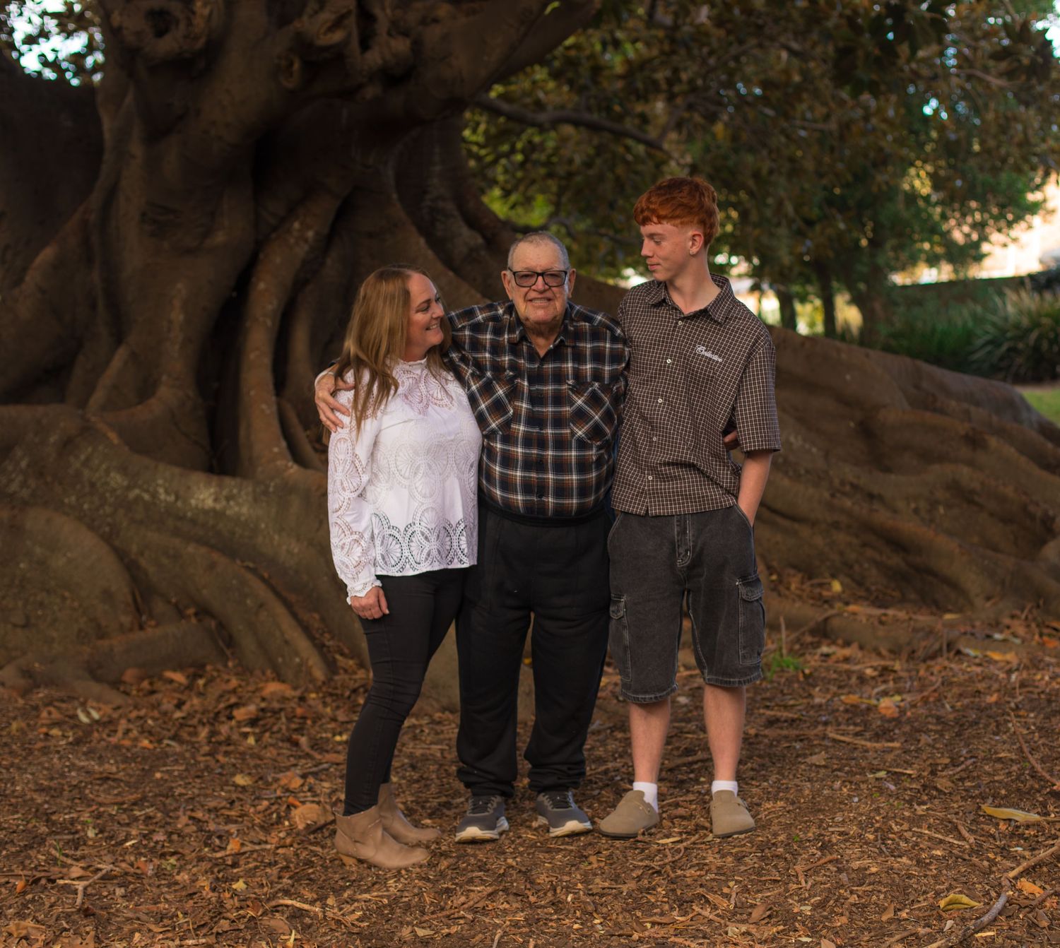 Son standing with his mum and grandad beneath a large tree during a three-generation family photography session.