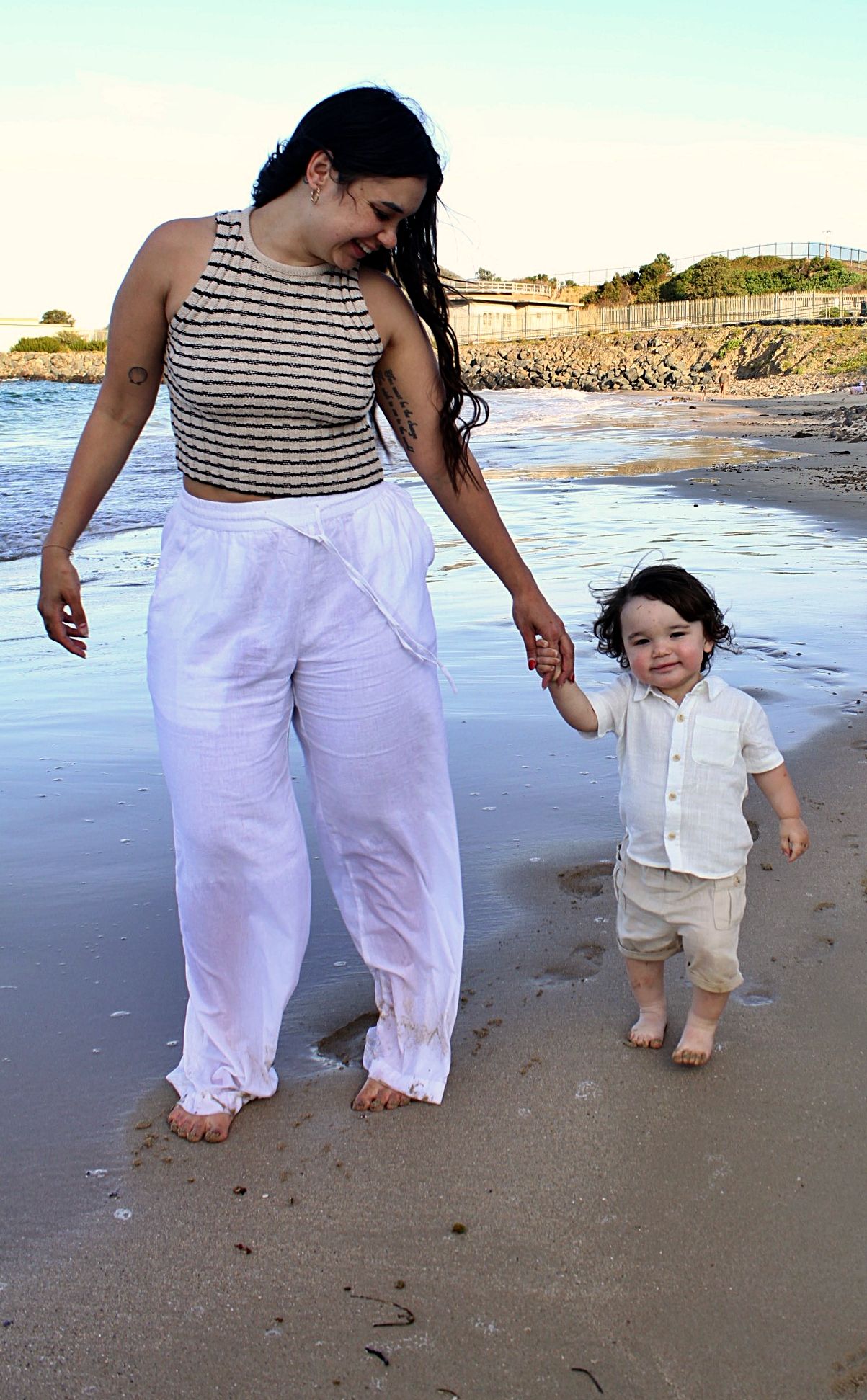 Beach motherhood session showing a mother and son holding hands while walking along the shoreline.