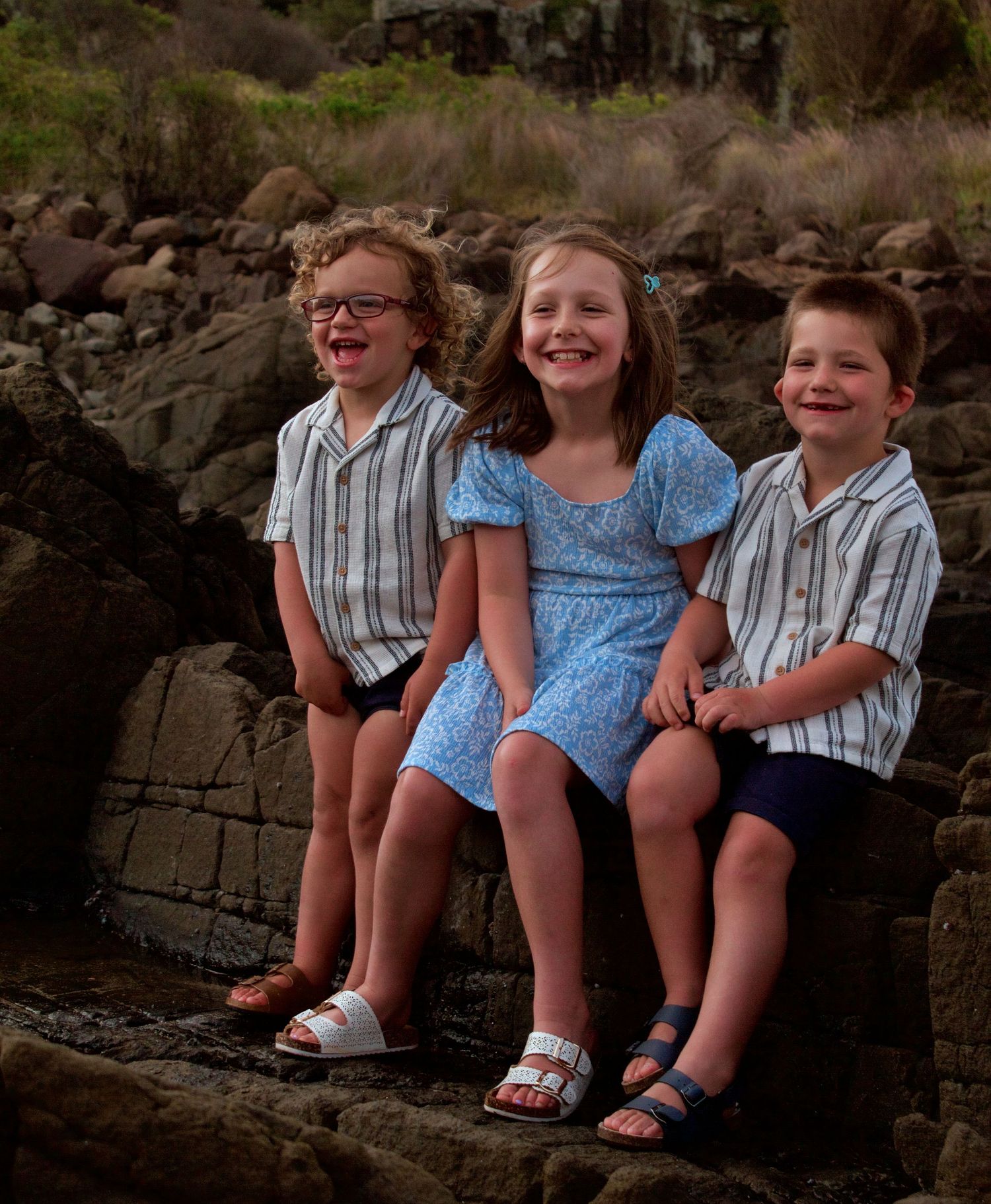 Candid moment of three children giggling on natural rocks during an outdoor lifestyle family session.