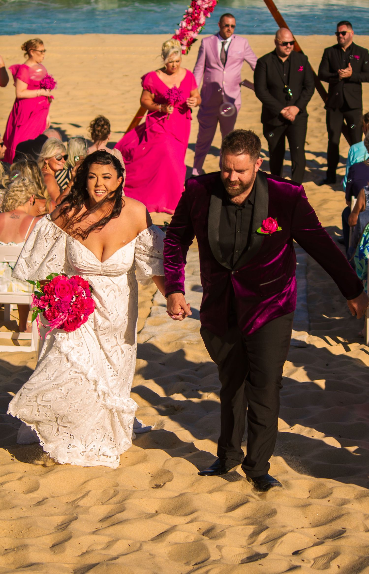 Bride and groom walking away from the ceremony together as newlyweds on the beach.
