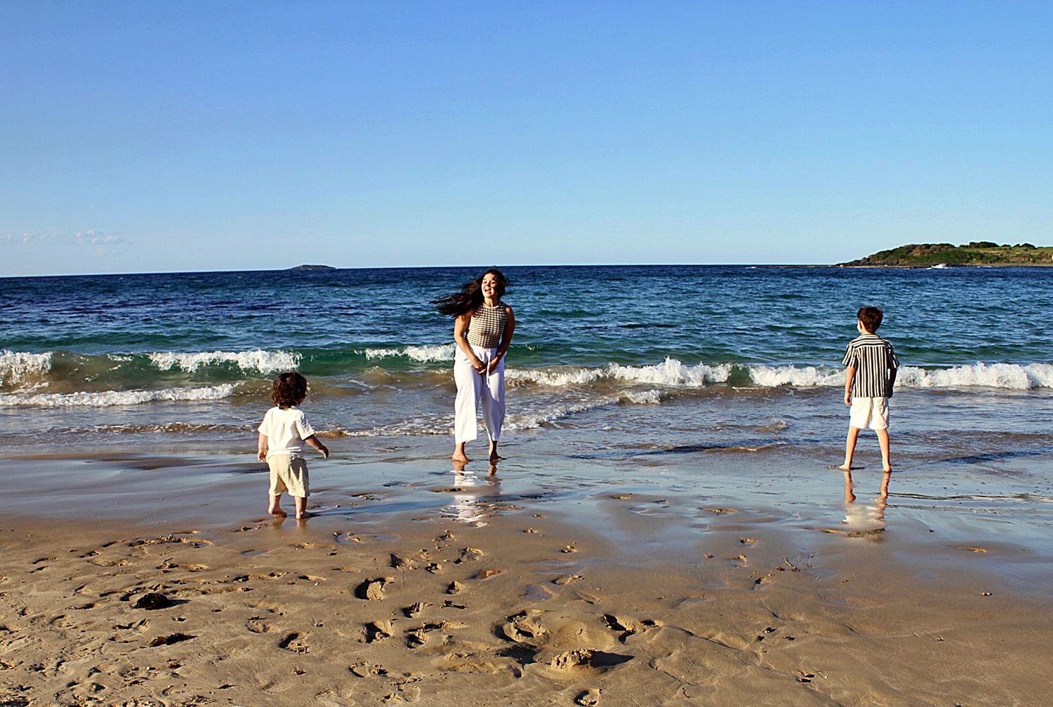 Candid motherhood photography session on the beach featuring a mum and her three boys enjoying the shoreline together.