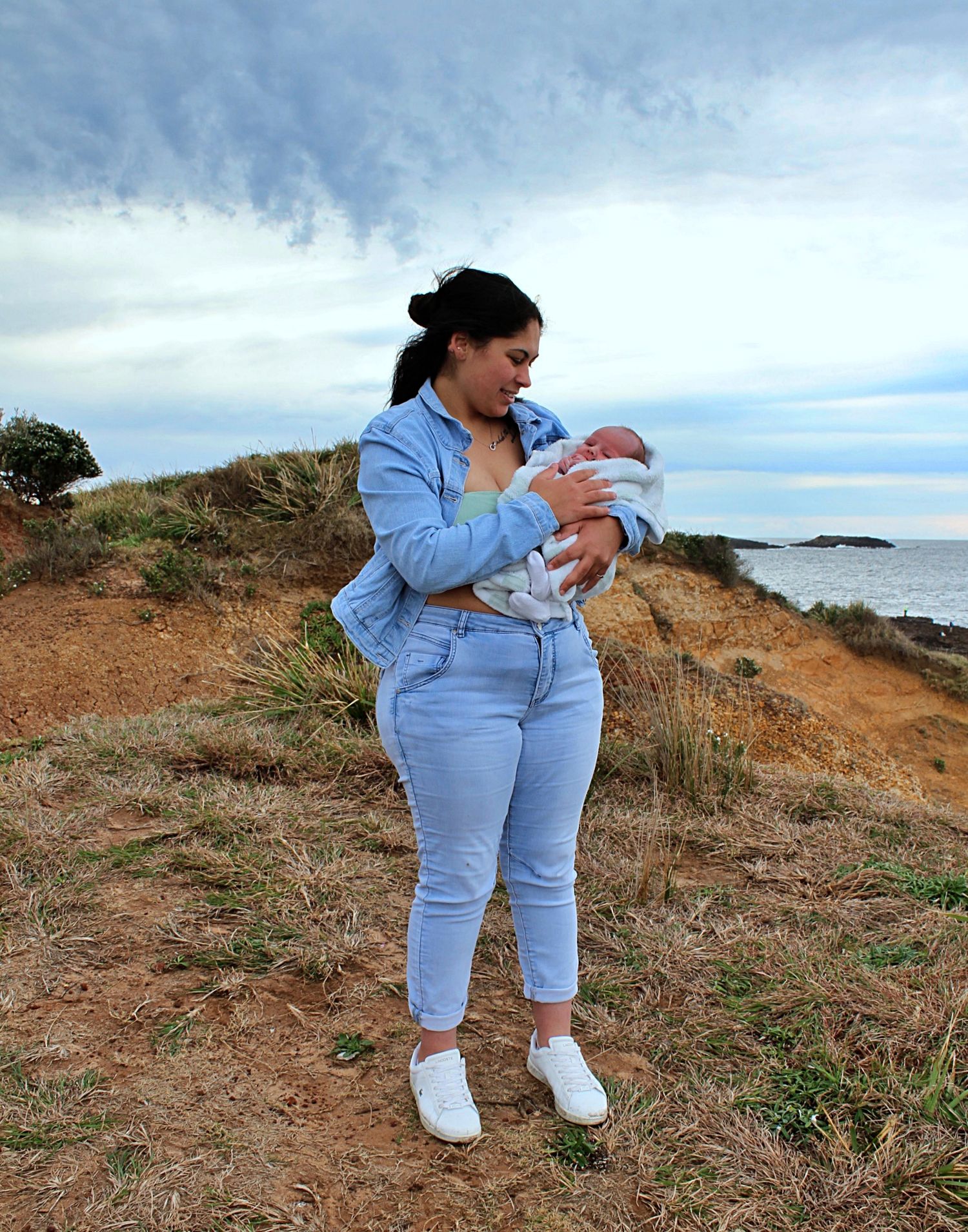 Mum cuddling her newborn baby with the ocean in the background in the Illawarra, taken by A Lasting Impression Photography.