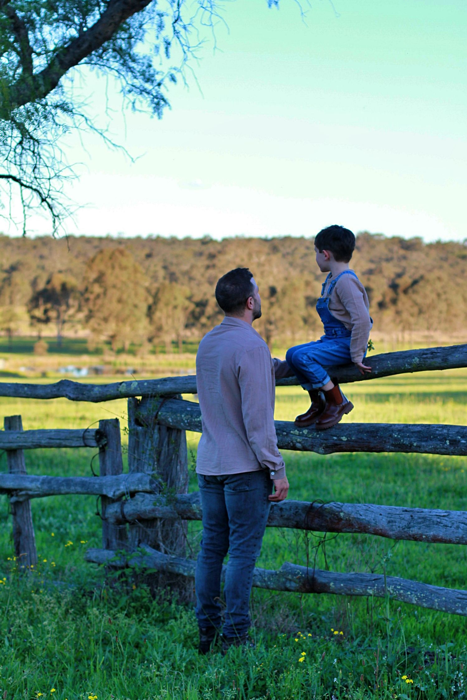 Boy climbing a wooden fence with help from an adult during a family session